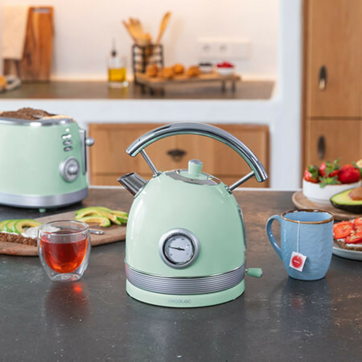 Miętowy czajnik elektryczny i toster, z niebieskim kubkiem i śniadaniem na stole.