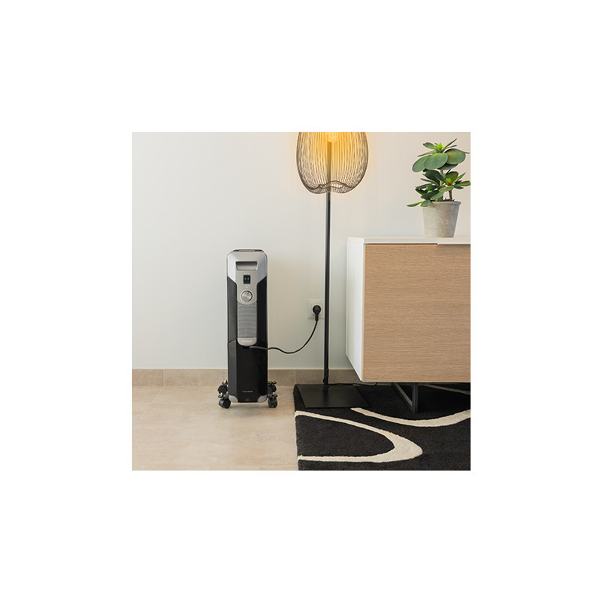 Czarny grzejnik elektryczny na kółkach, w pobliżu ściany, dywanu i lampy podłogowej.