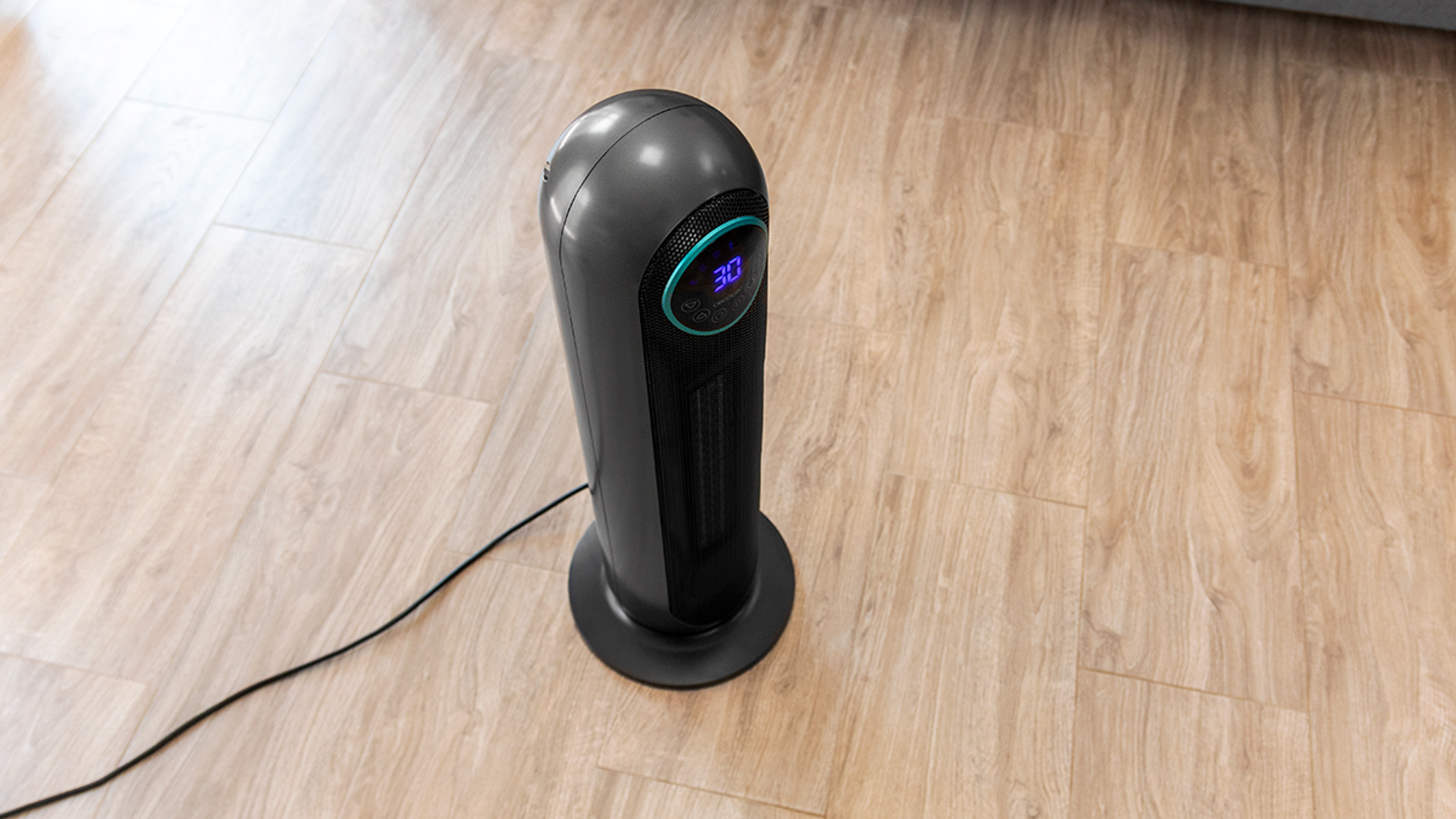 Czarny grzejnik elektryczny na drewnianej podłodze. Elementy sterujące i wyświetlacz cyfrowy. Grzejnik jest wysoki i cylindryczny.