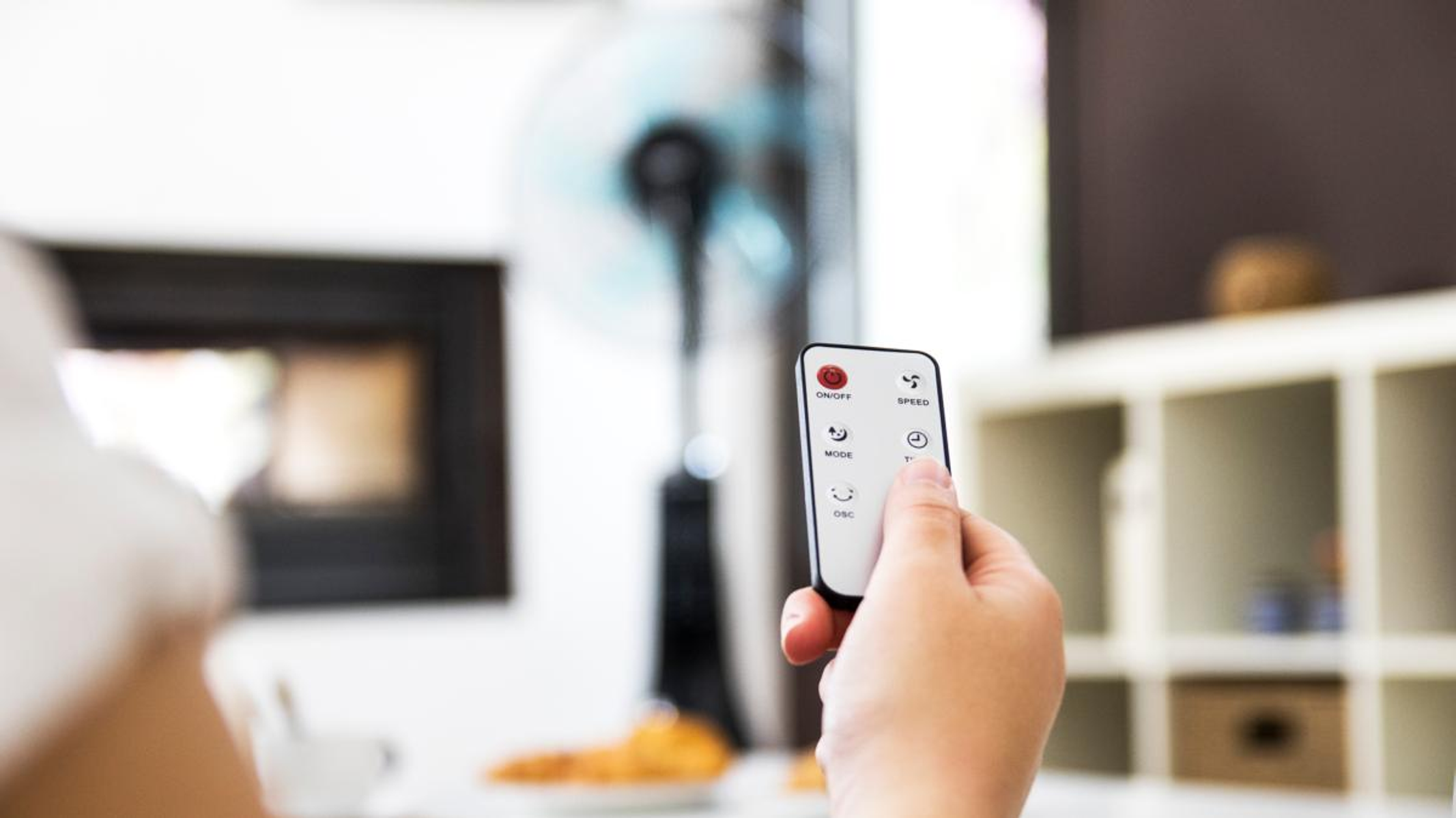 Mano che tiene un telecomando per un ventilatore. Pulsanti per accensione, modalità e velocità visibili.