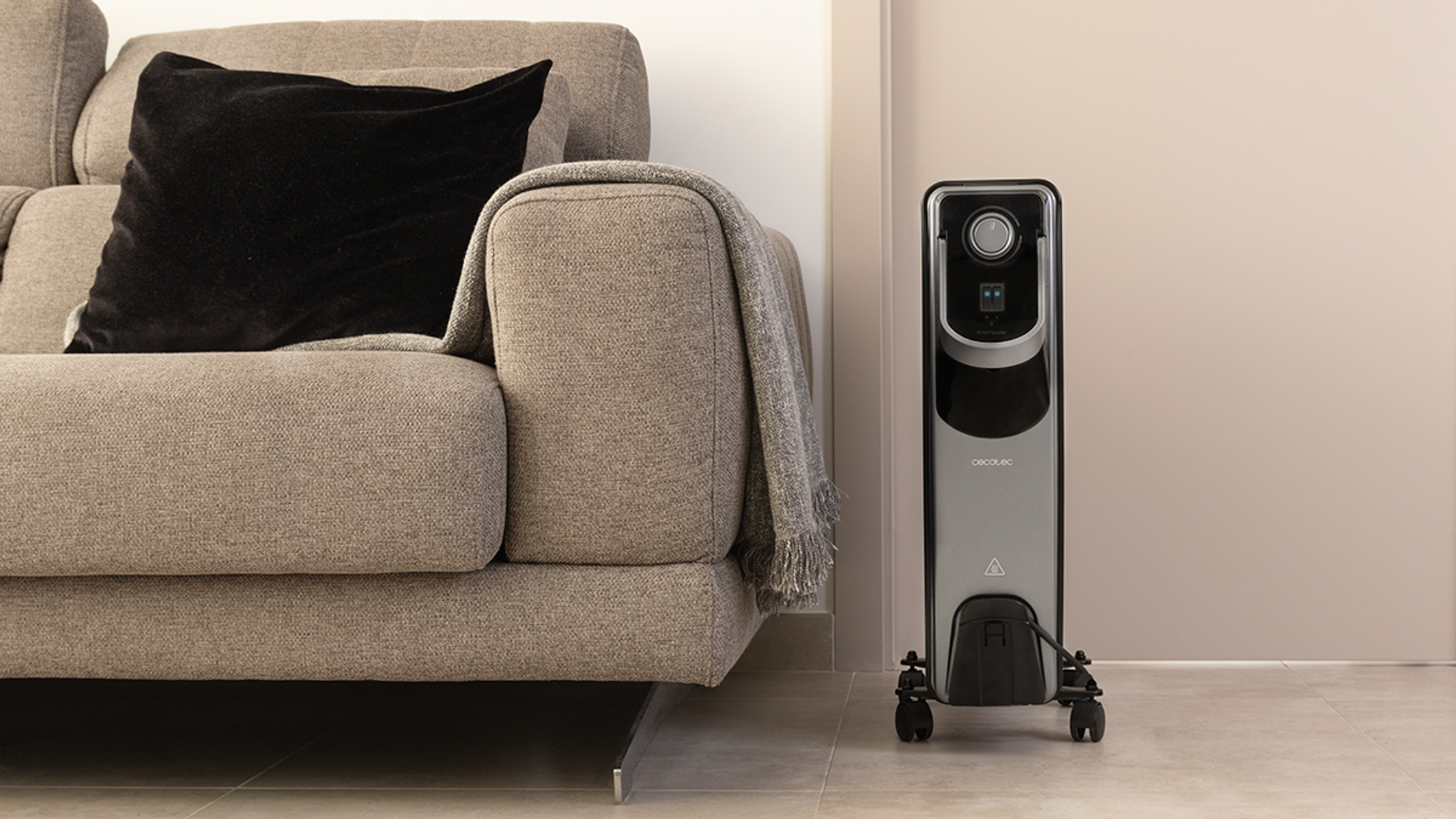 Szara kanapa z czarną poduszką i szarym kocem. Czarny grzejnik jest w pobliżu.