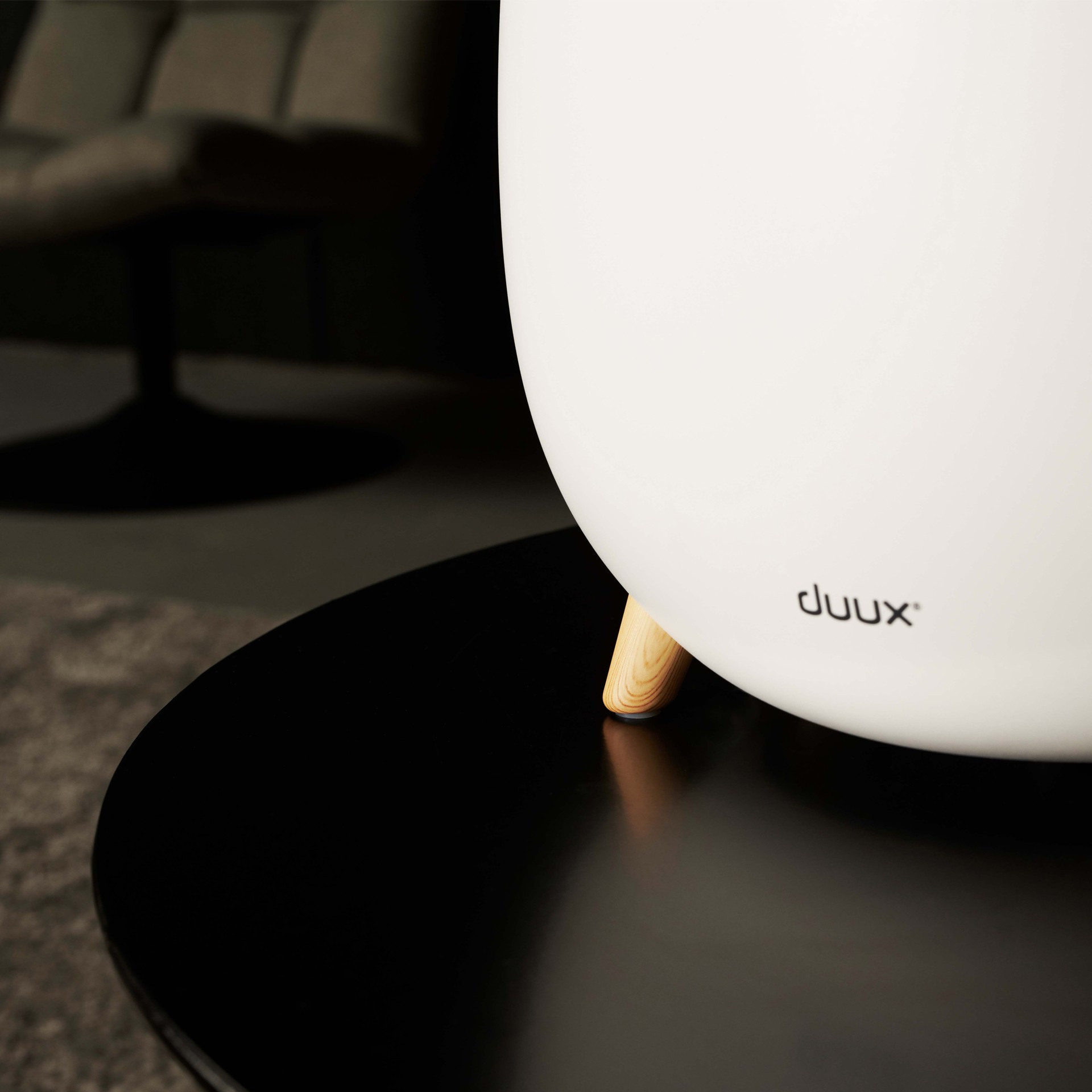 Biały nawilżacz powietrza na czarnym stole z drewnianymi nogami. Szare krzesło w tle.