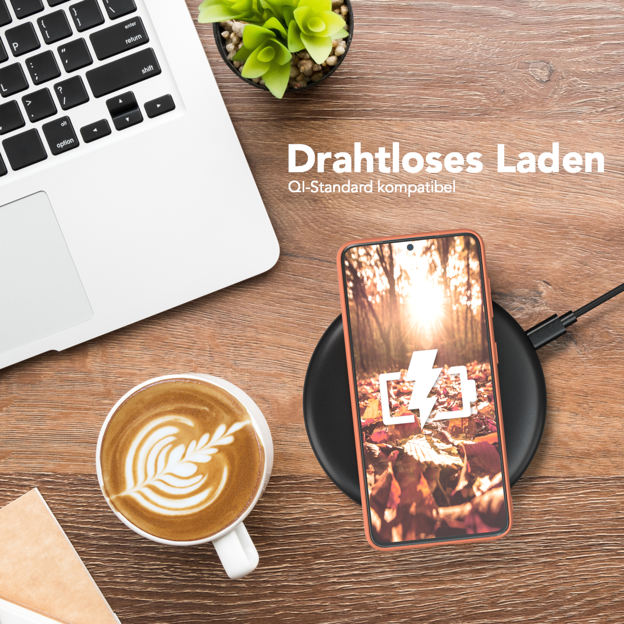 Laptop, Kaffee, Handy auf kabellosem Ladegerät. Handy zeigt Blätter, Ladesymbol. Holztisch, grüne Pflanze im Hintergrund.