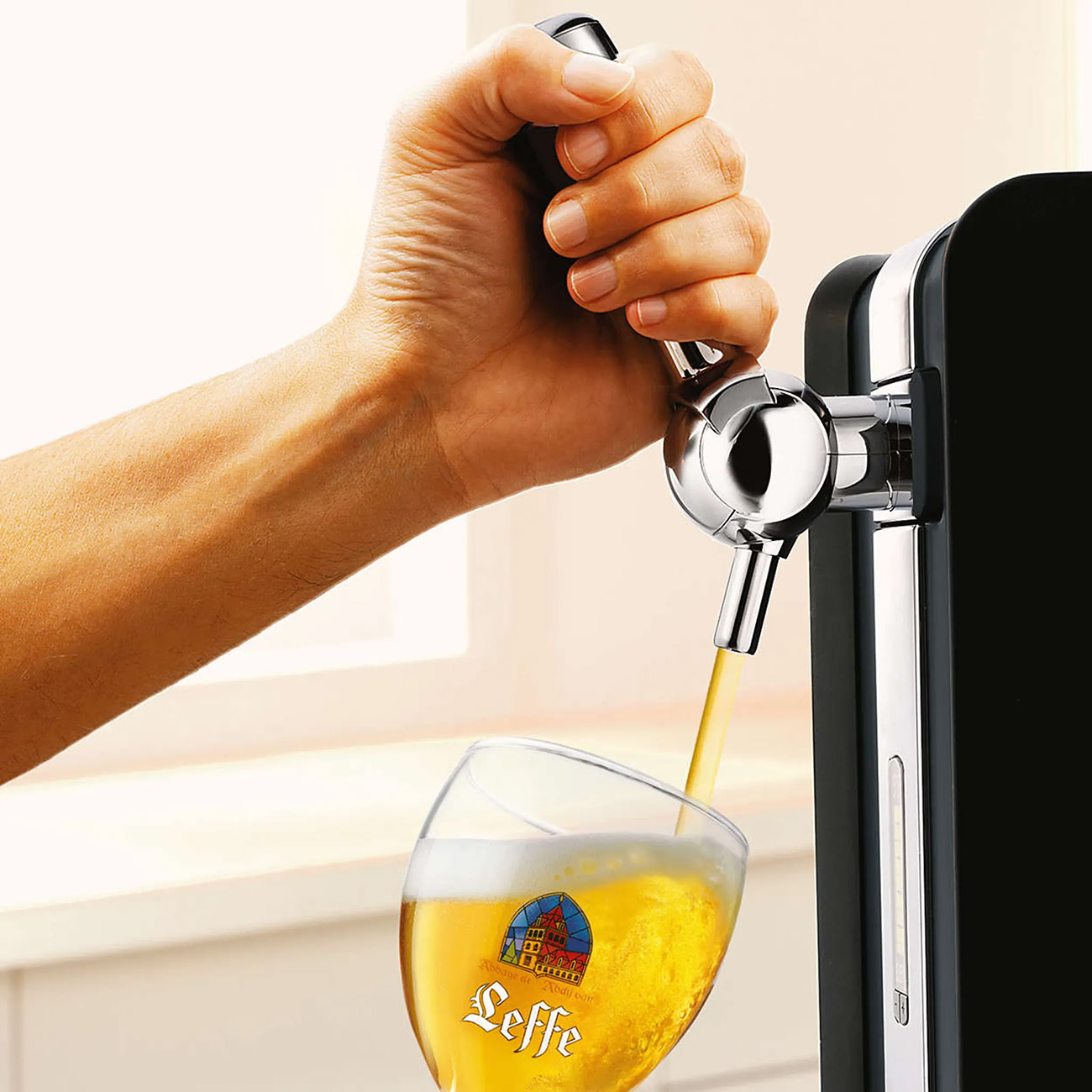 Una mano versa birra da un rubinetto in un bicchiere con il logo Leffe, in un ambiente ben illuminato.