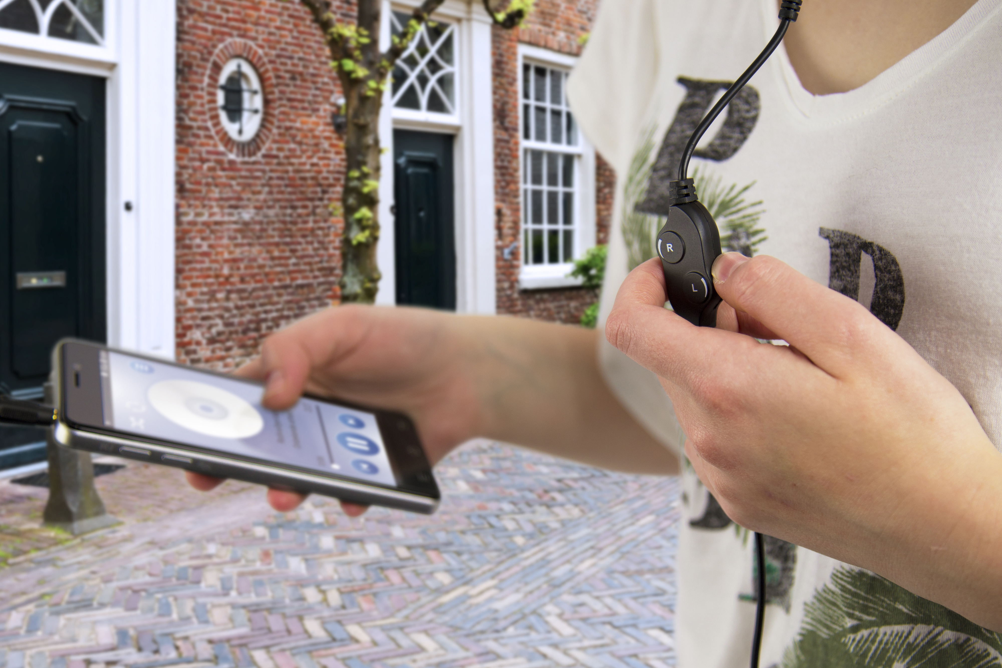Person mit Kopfhörern hält ein Telefon, geht auf Kopfsteinpflaster.