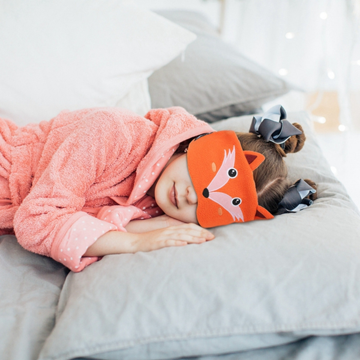 Mädchen schläft auf einem Kissen, trägt eine Fuchs-Augenmaske und einen rosa Bademantel.