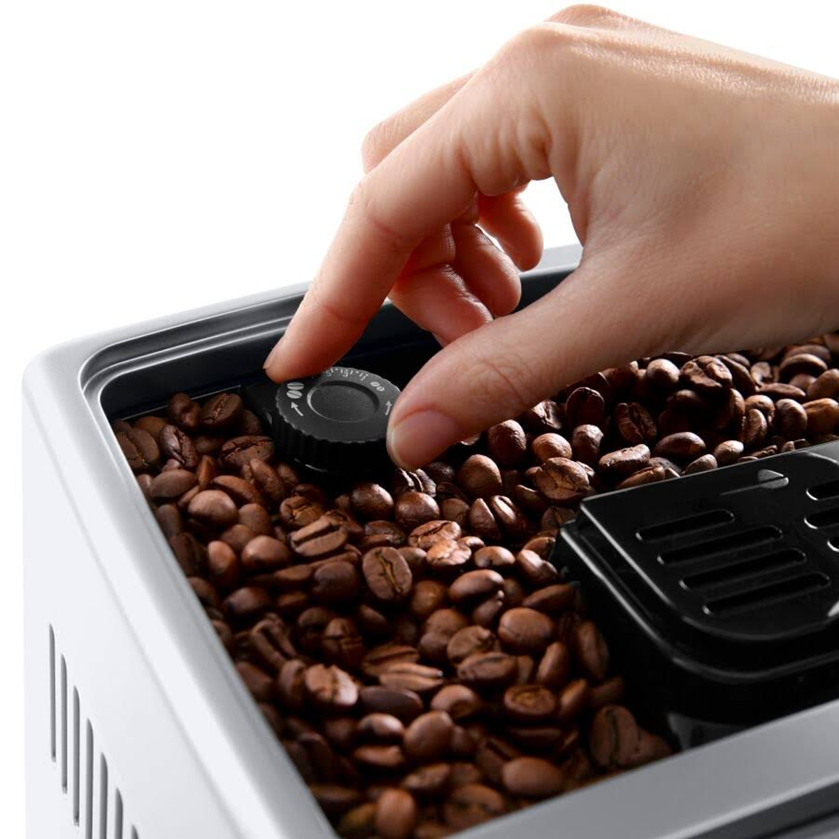 Ręka kręci pokrętłem w ekspresie do kawy wypełnionym ziarnami kawy.