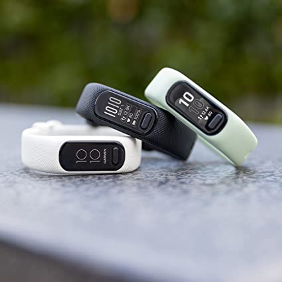 Three fitness trackers, black, white, and green, on a gray surface.