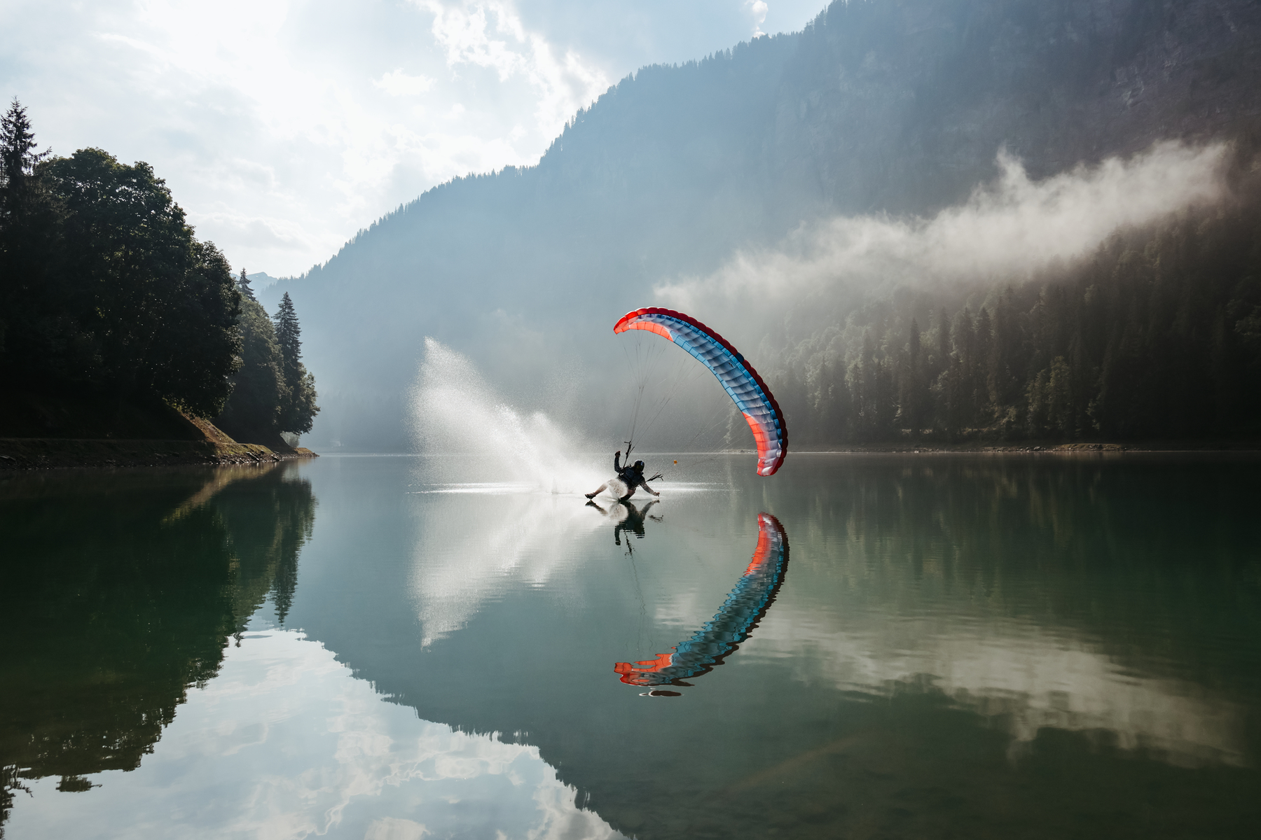 Paraglider over a lake with mountains in the background.