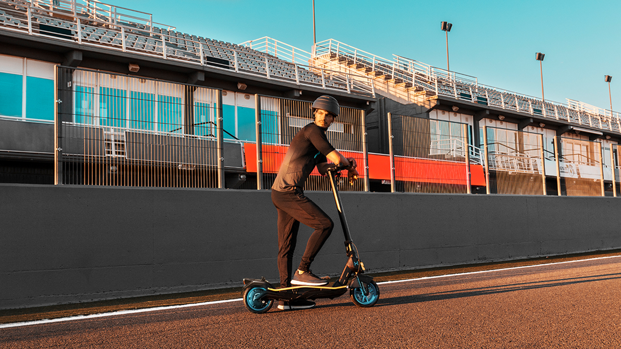 Un uomo su un monopattino elettrico su una pista, indossa un casco e abiti sportivi.