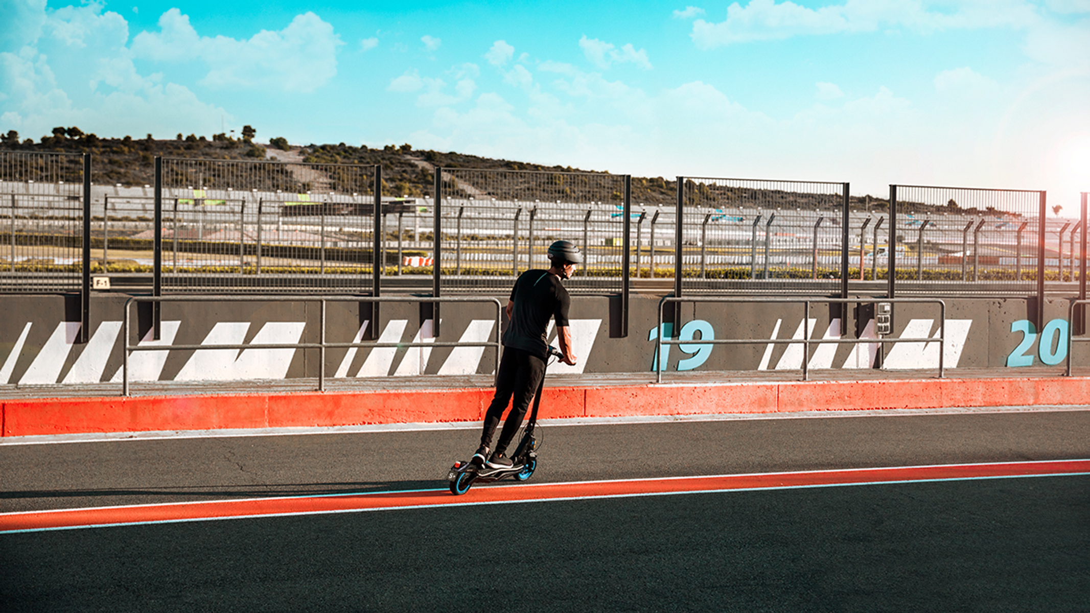 Uomo in scooter su una pista. Cielo blu e barriere sullo sfondo.