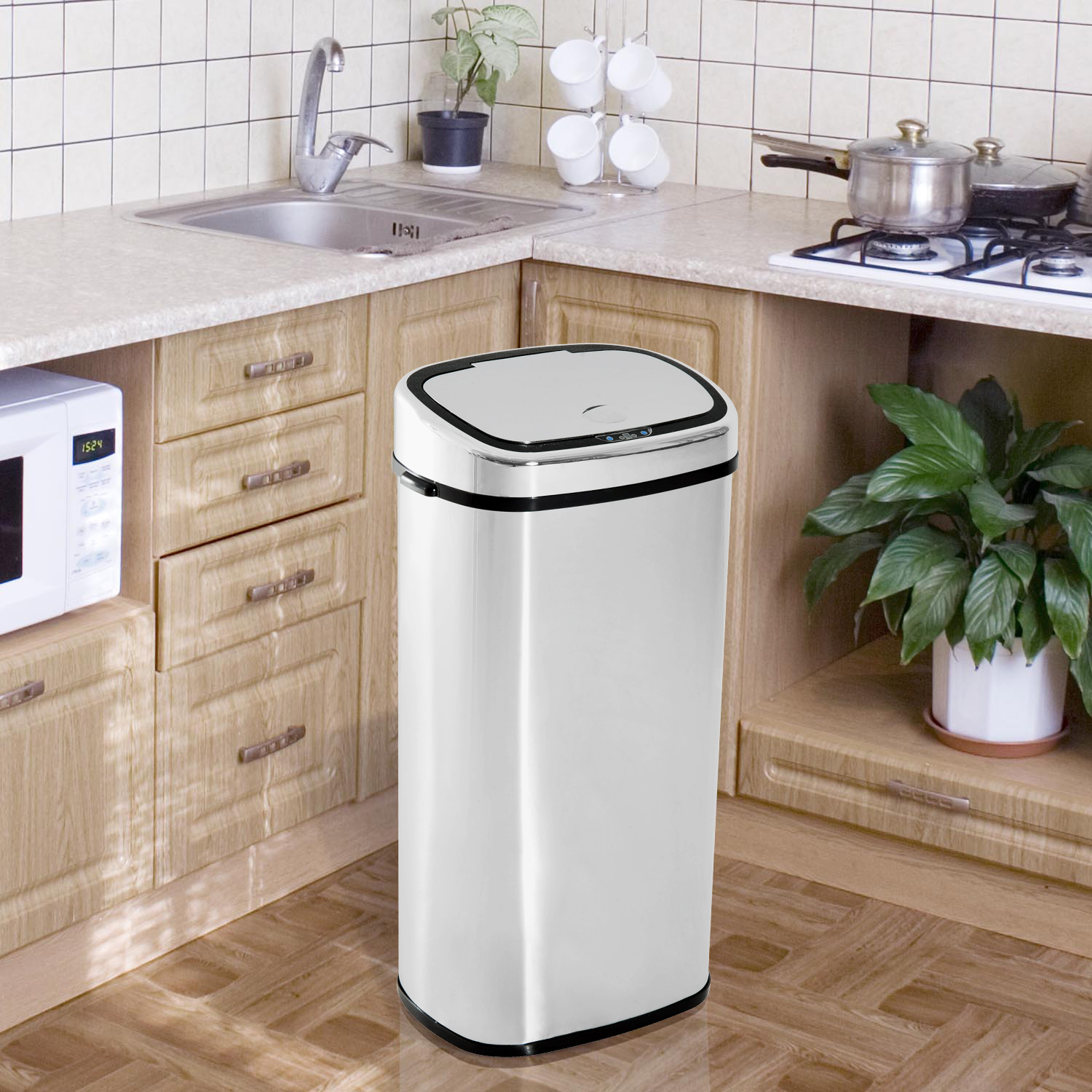 Contenedor de basura de acero inoxidable con tapa negra. Está en un entorno de cocina con fregadero y armarios.