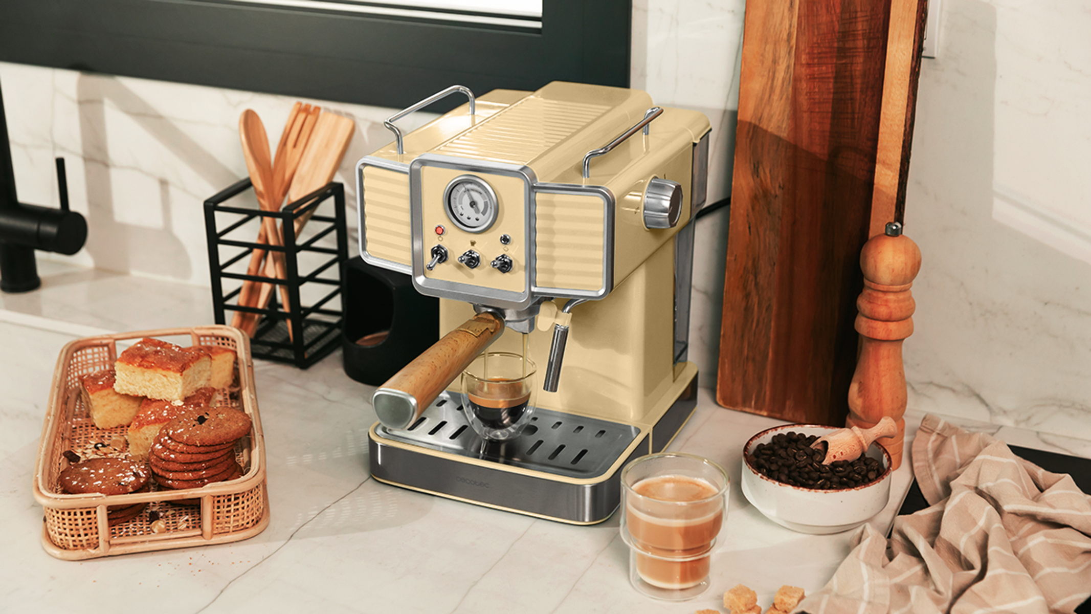 Una cafetera beige con un vaso de espresso en la encimera, con otros accesorios de café.