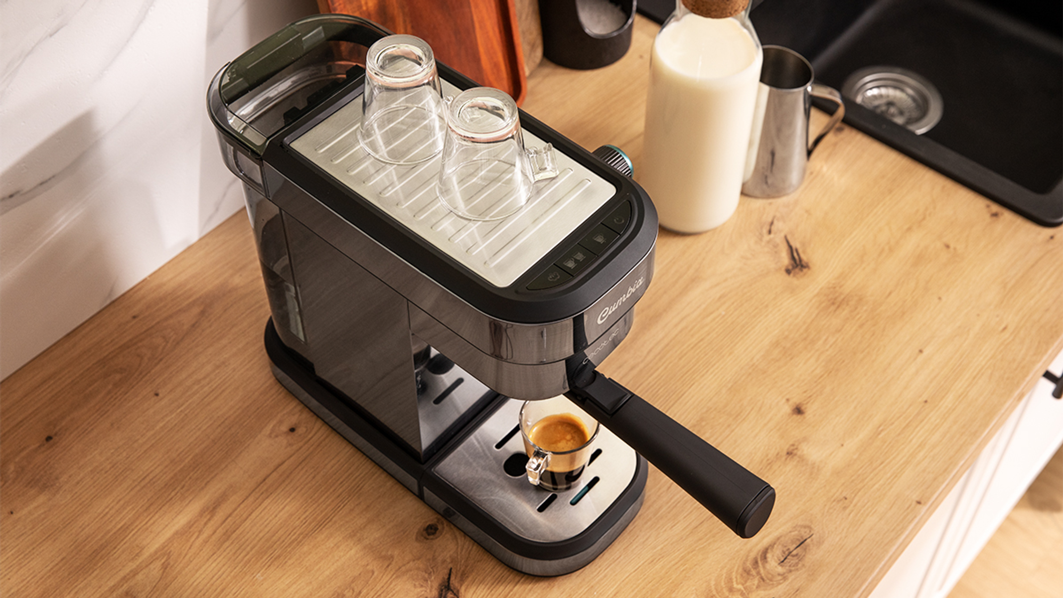 Ekspres do kawy na drewnianej powierzchni z dwoma szklankami, dzbankiem do mleka i nalewanym espresso.