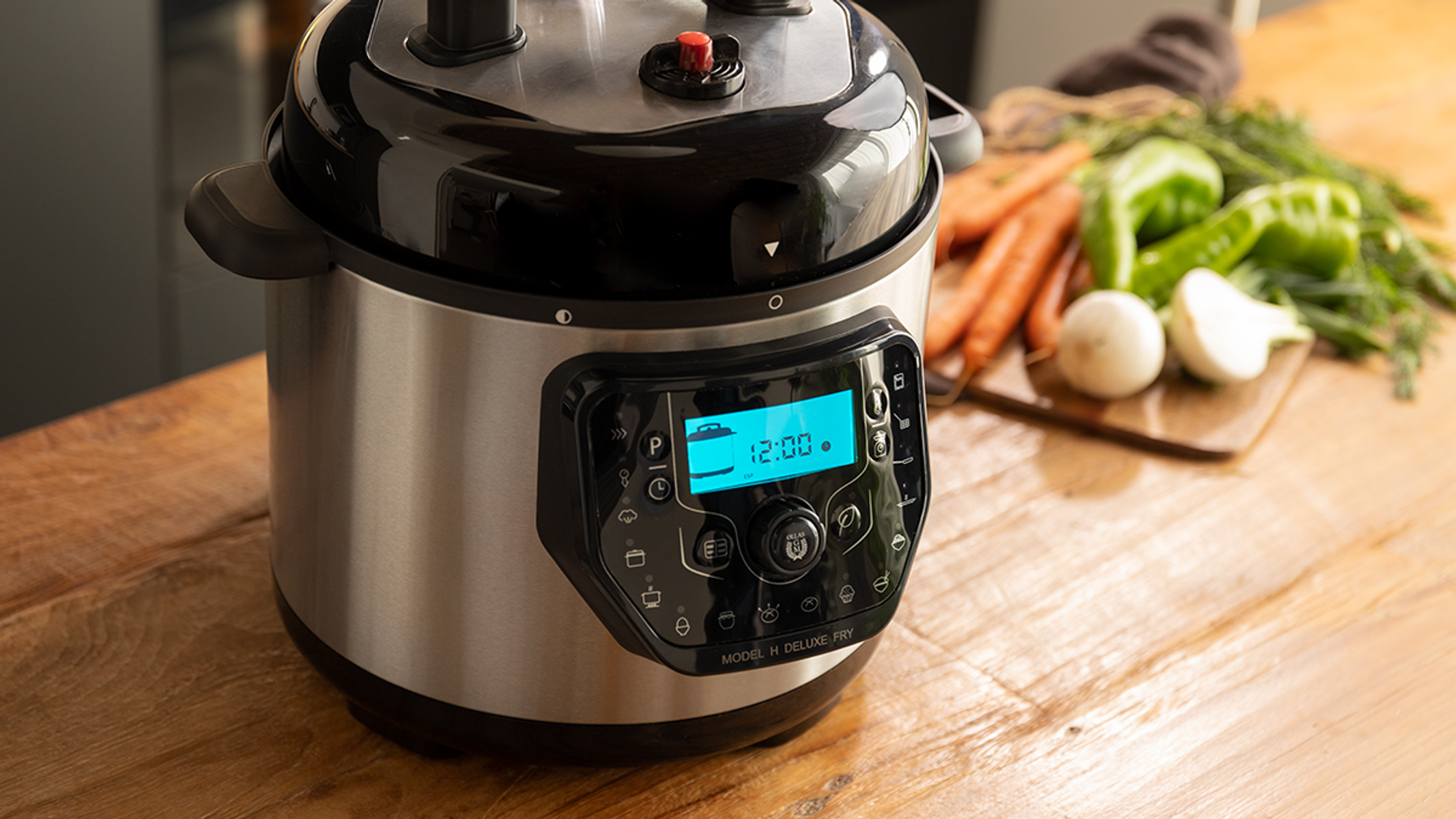 Una olla a presión con pantalla digital, rodeada de verduras sobre una mesa de madera.