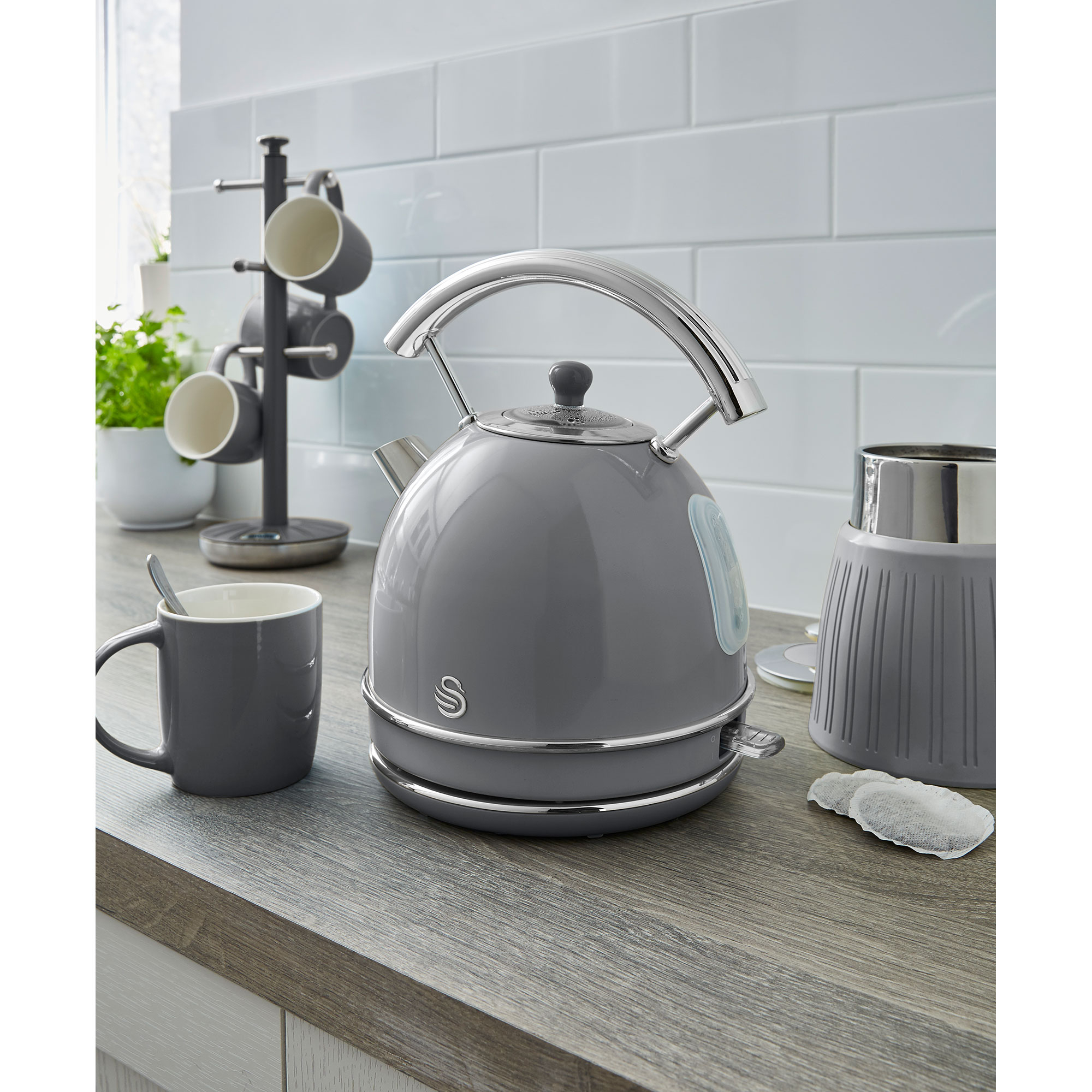 Una tetera gris sobre una encimera de madera con una taza y un recipiente para té.