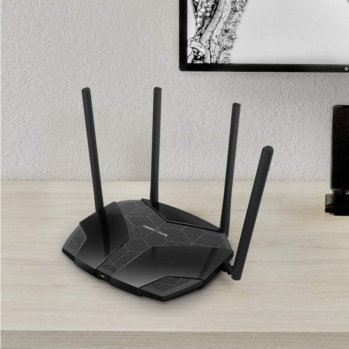 Een zwarte router met vier antennes op een houten tafel, met een schilderij en een telefoon op de achtergrond.