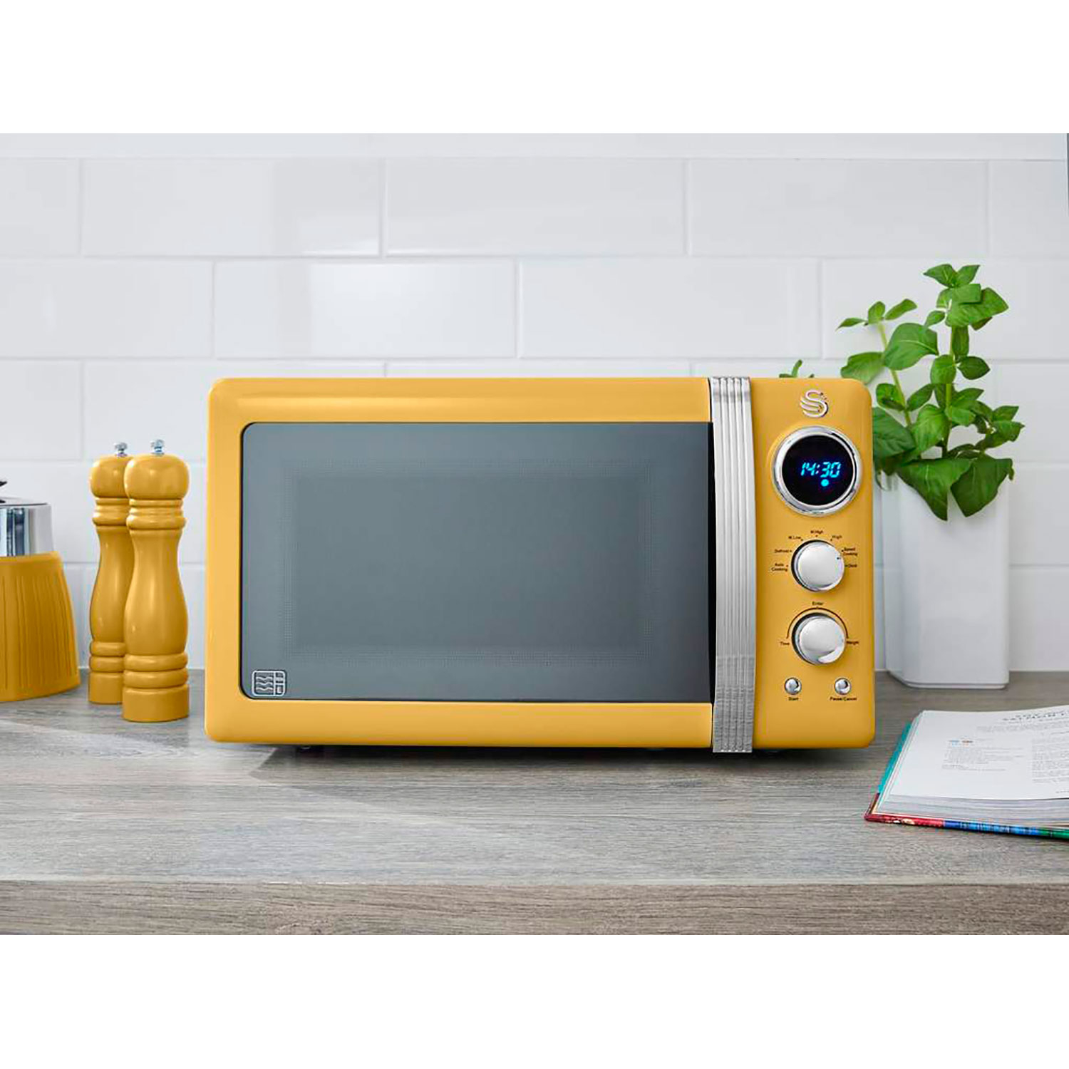 Microondas amarillo sobre una encimera con pantalla de reloj, salero y pimentero, y una planta.