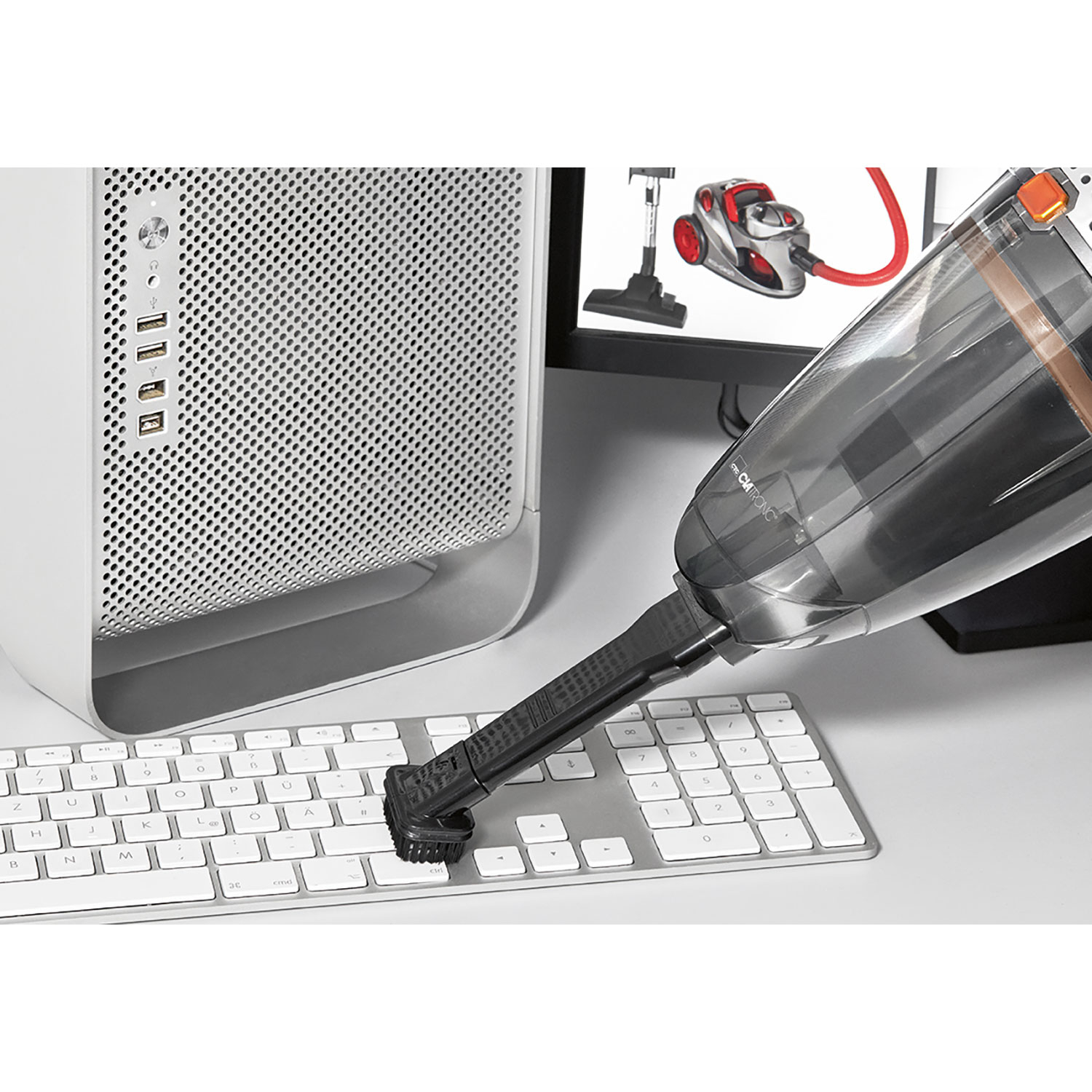 Odkurzacz ręczny czyszczący klawiaturę. W tle komputer i monitor.