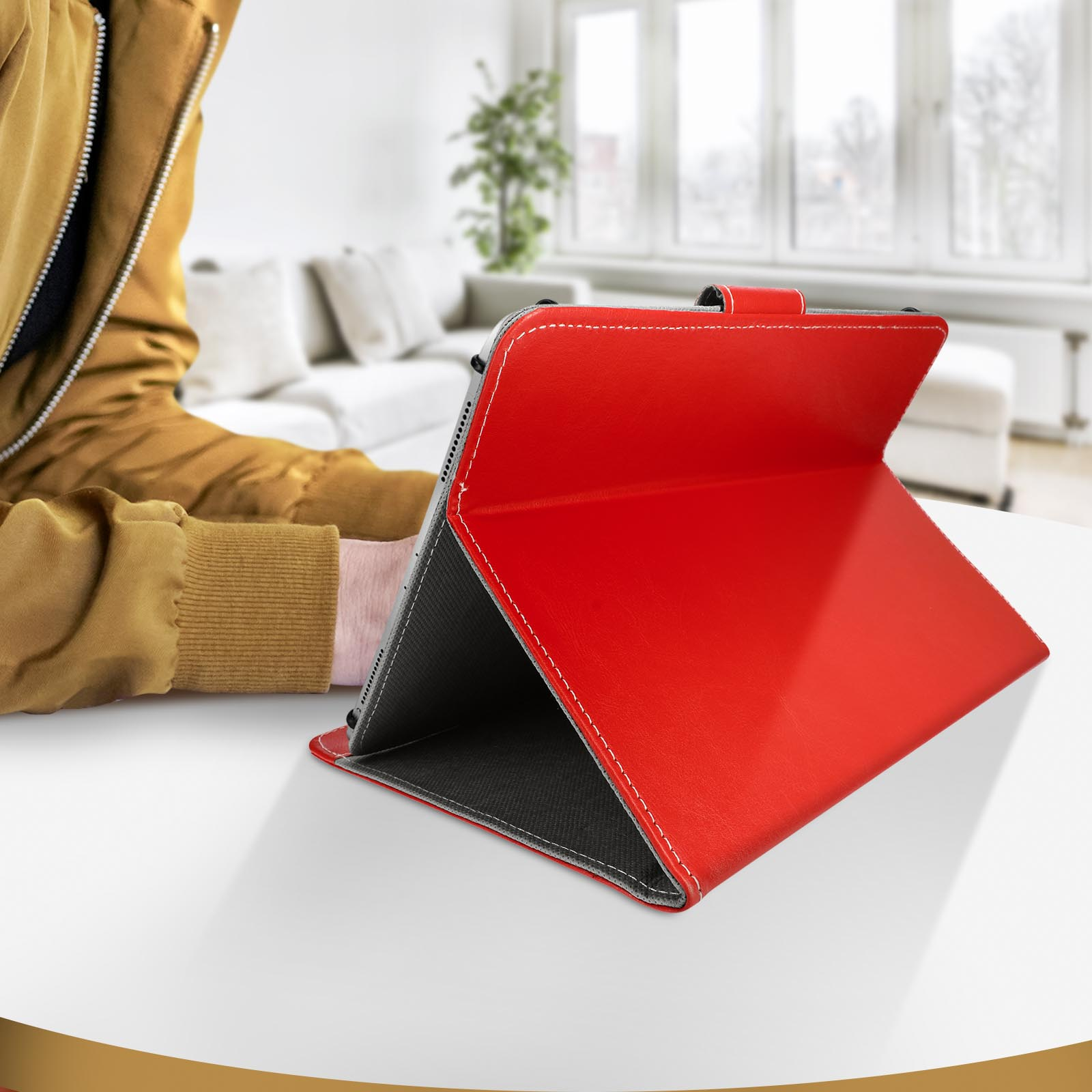 Tablet in una custodia rossa, aperto su un tavolo bianco. Una persona è seduta vicino, con un maglione giallo.