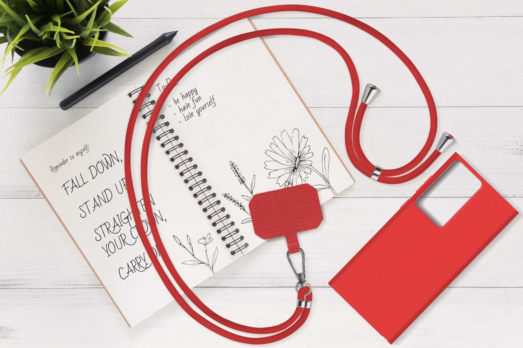 Rotes Telefon-Lanyard mit roter Handyhülle, Notizbuch und Stift auf einem Holztisch.