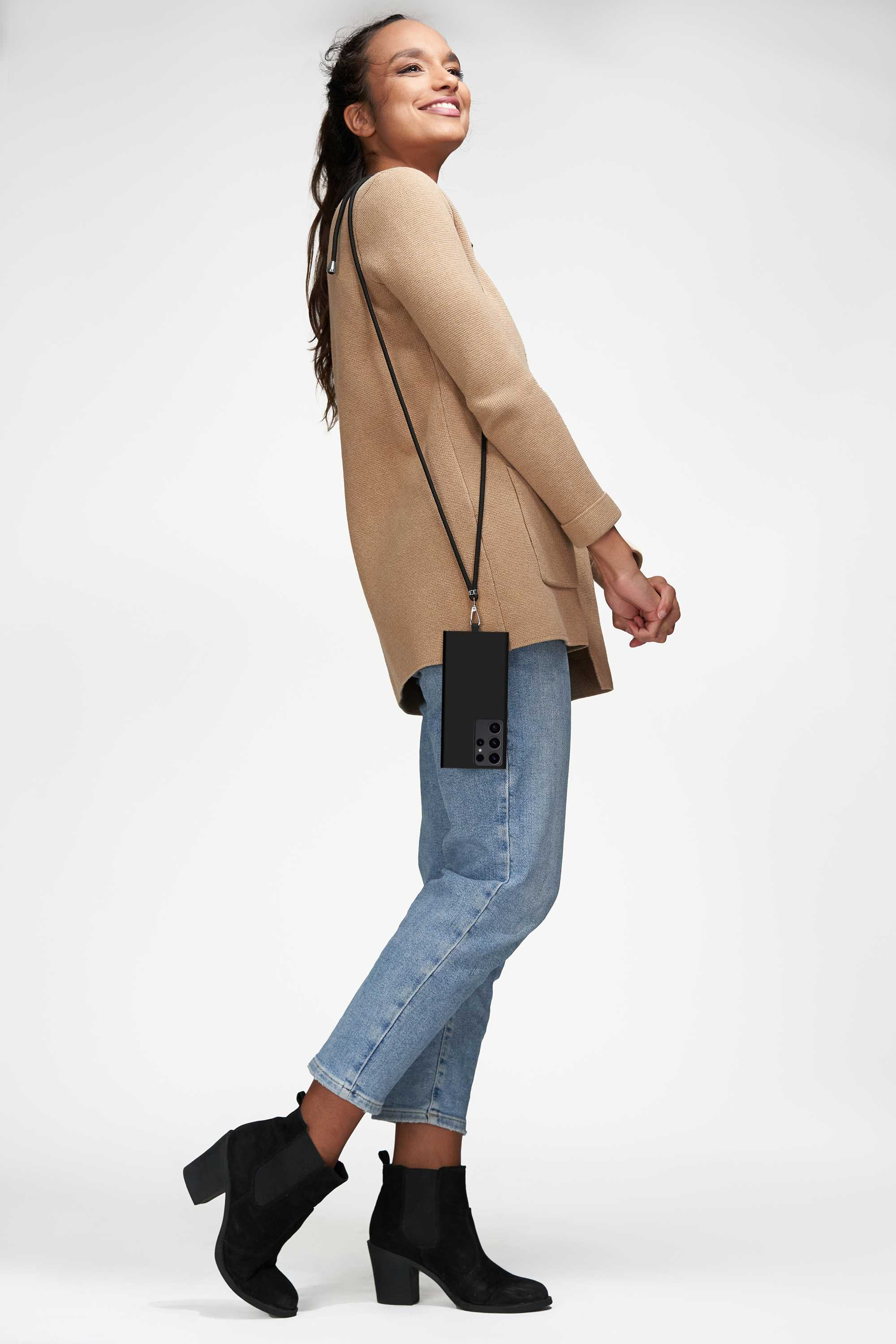 Eine Frau mit Handyhülle, hält ein Telefon mit Band, trägt eine beige Jacke und Jeans.