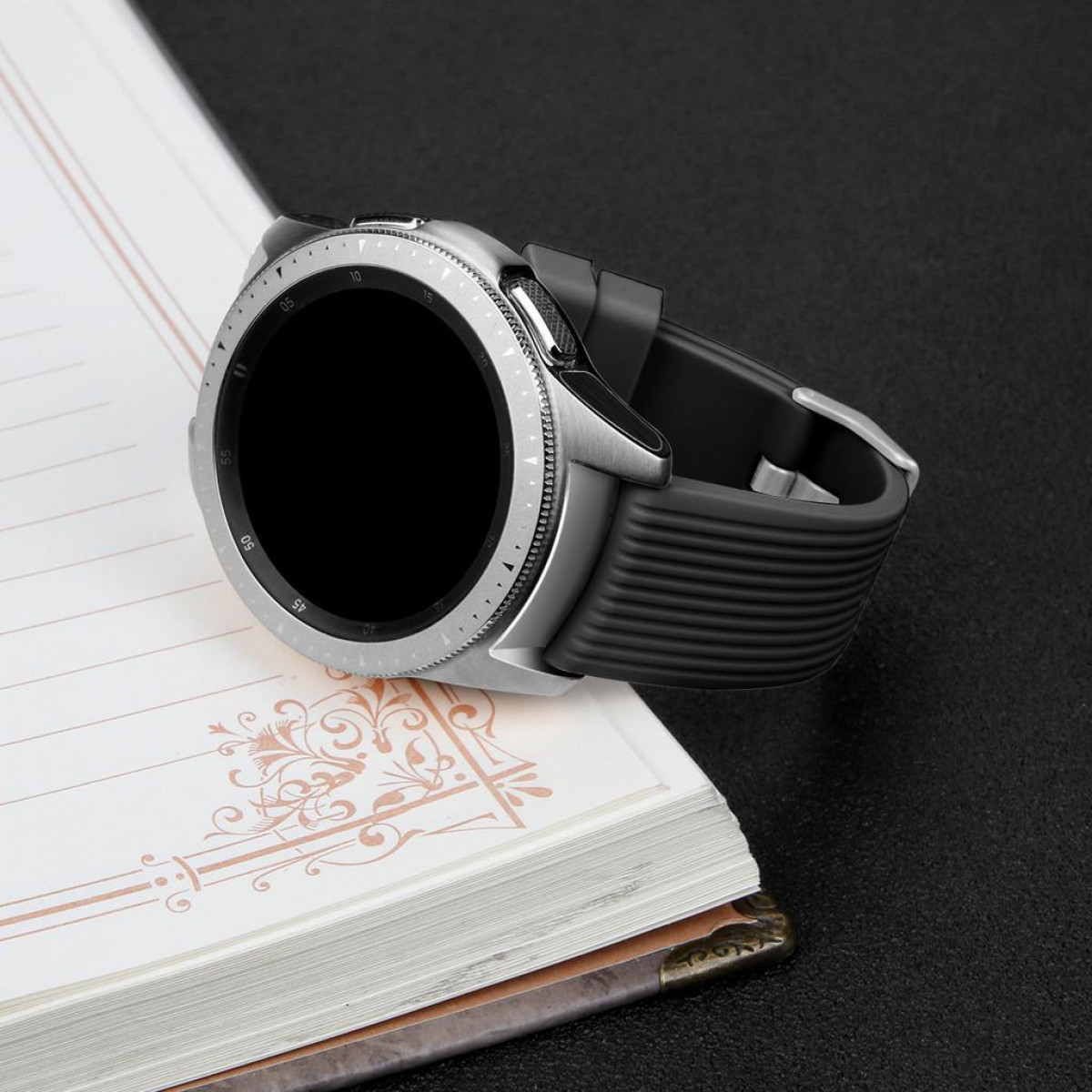 Smartwatch na notatniku. Czarny pasek, srebrna ramka.