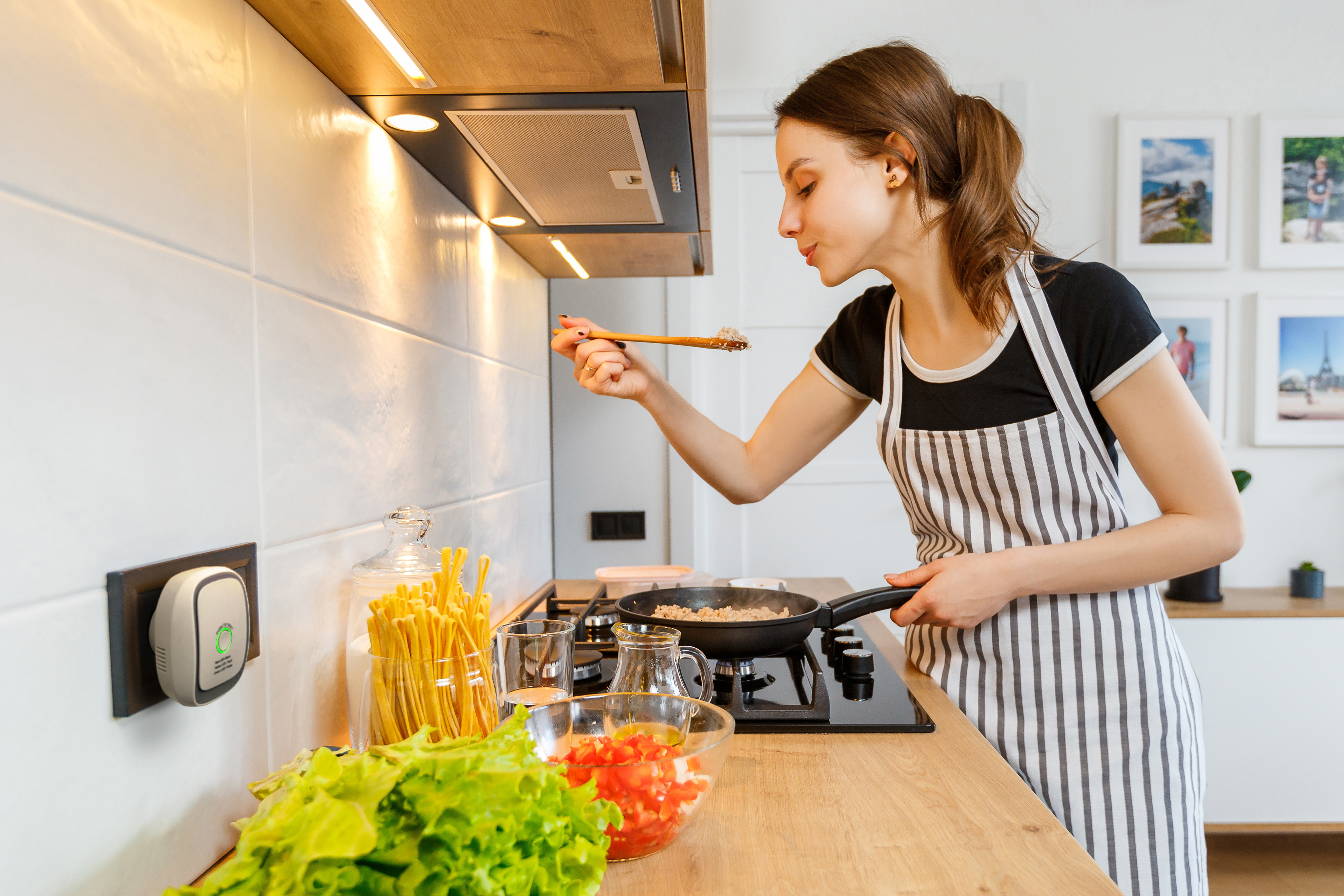 Frau in Küche, die Essen aus der Pfanne probiert. Küche mit weißen Fliesen und Theke.