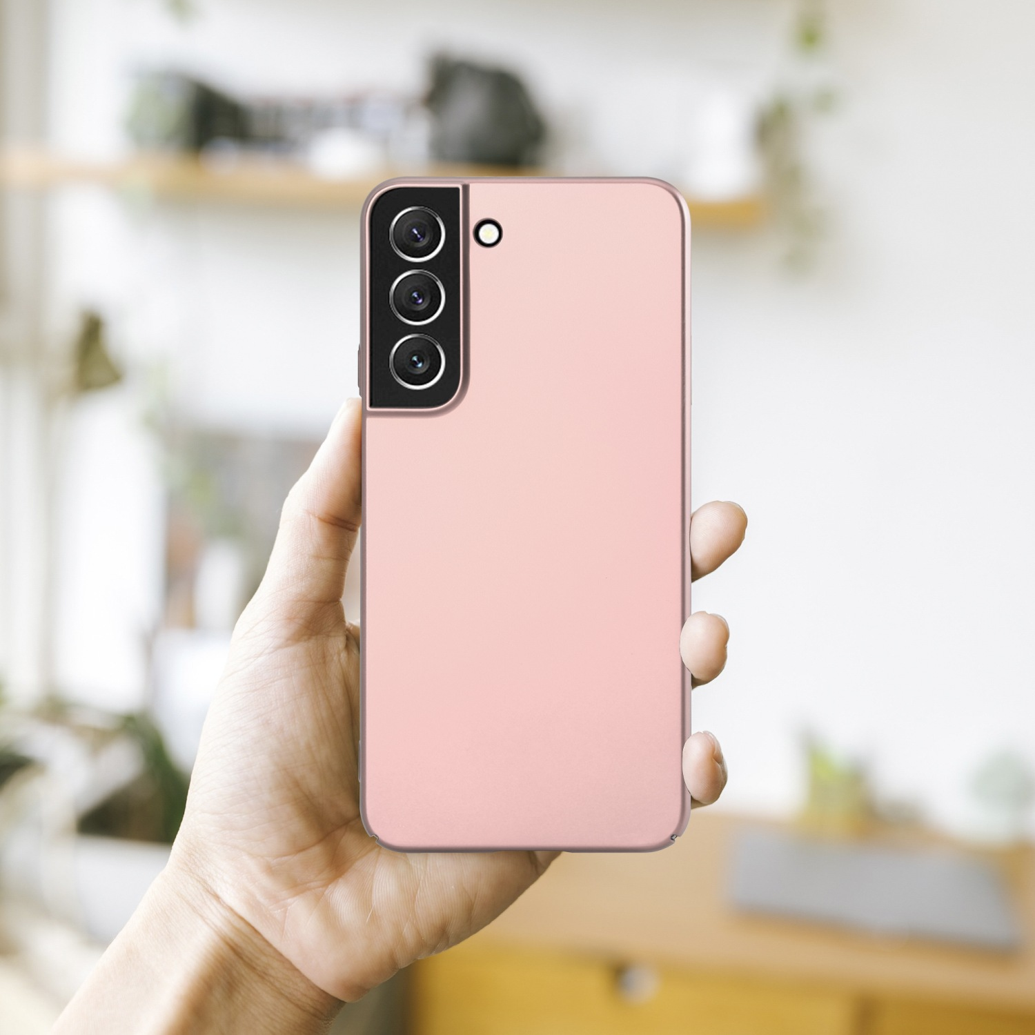 Die Hand einer Person, die ein pinkfarbenes Telefon mit drei Kameras auf der Rückseite hält. Verschwommener Hintergrund.