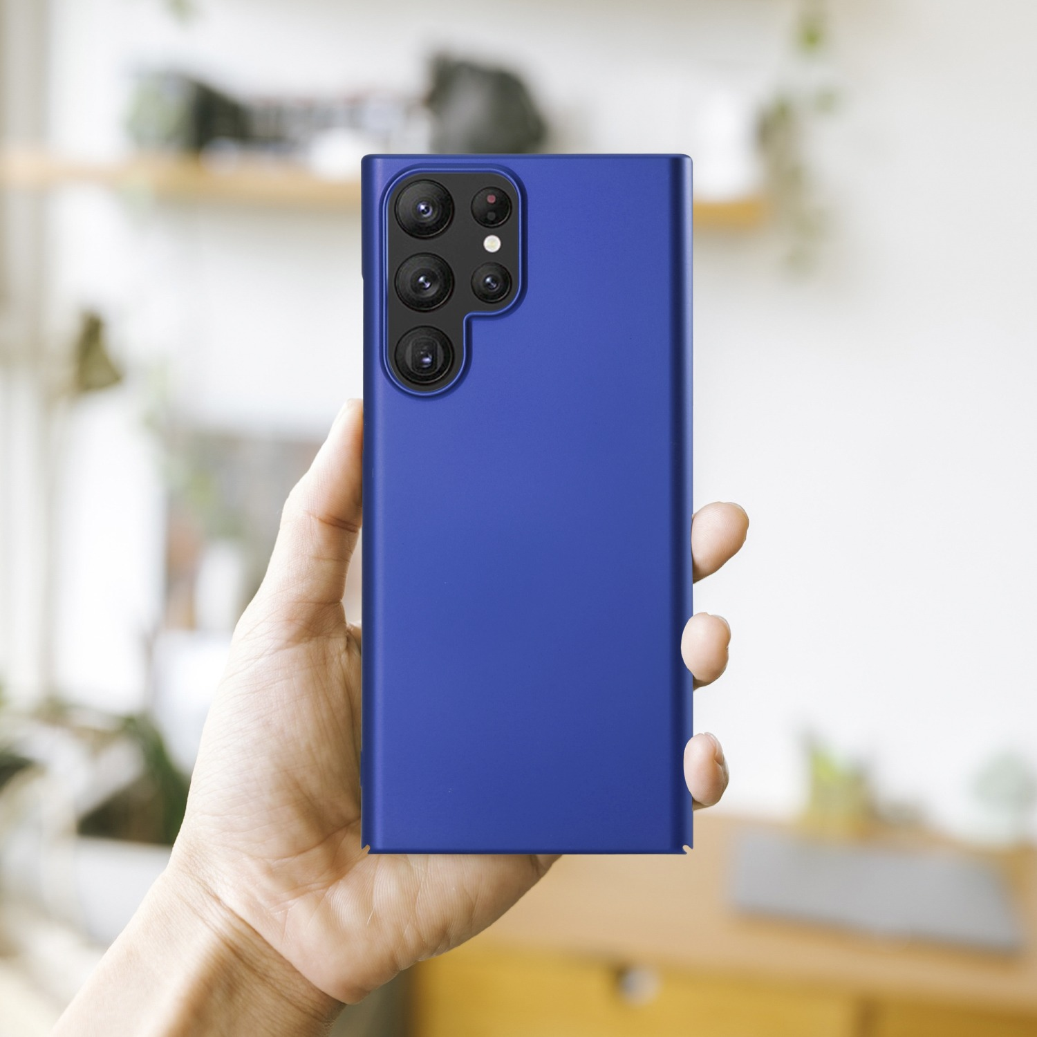 Hand, die ein blaues Telefon hält, zeigt die Rückseite mit Kameras auf unscharfem Hintergrund.