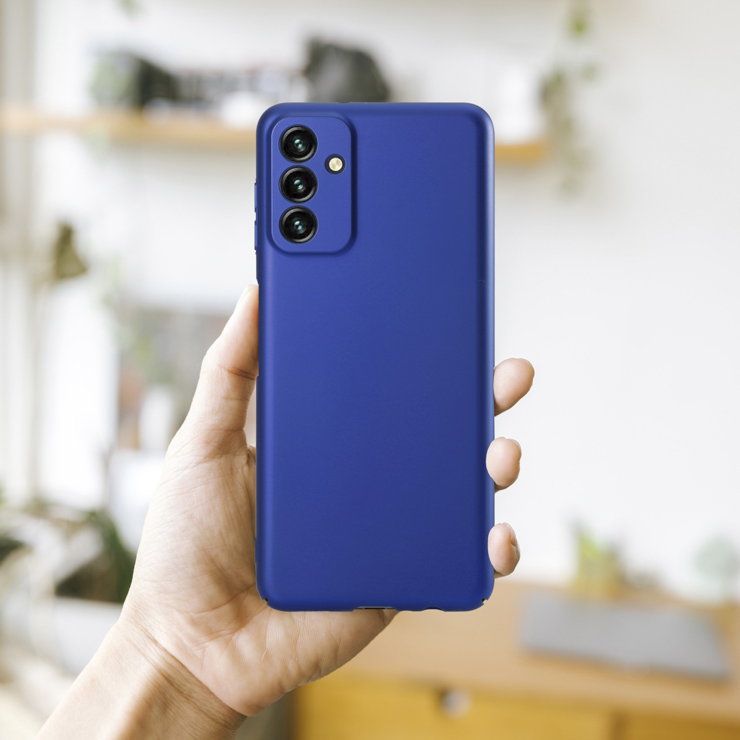 Eine Hand hält eine blaue Handyhülle. Die Hülle ist glatt, mit drei Kameralinsen. Ein unscharfer Hintergrund ist sichtbar.