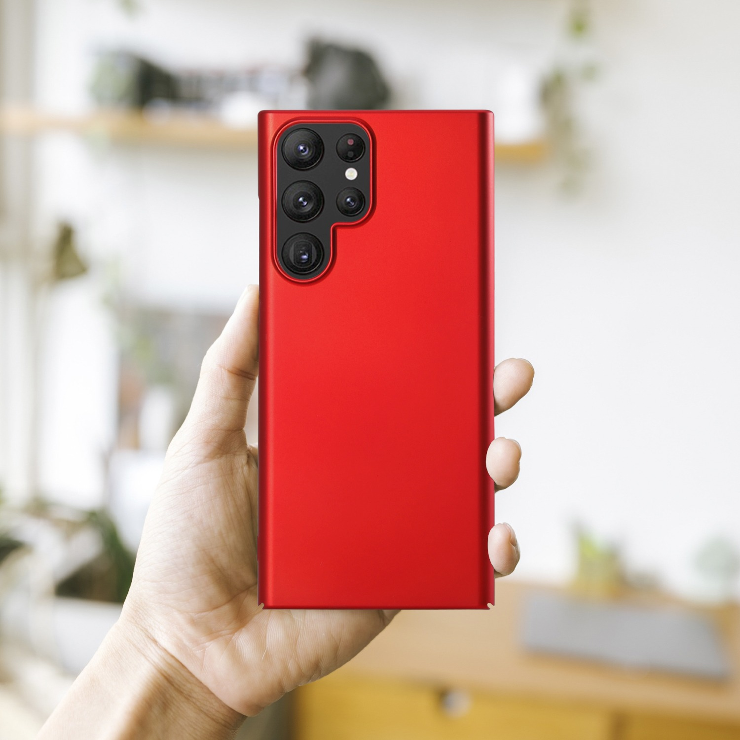 Hand hält ein rotes Telefon, Rückseite, mit mehreren Kameras. Hintergrund ist ein verschwommenes Interieur.