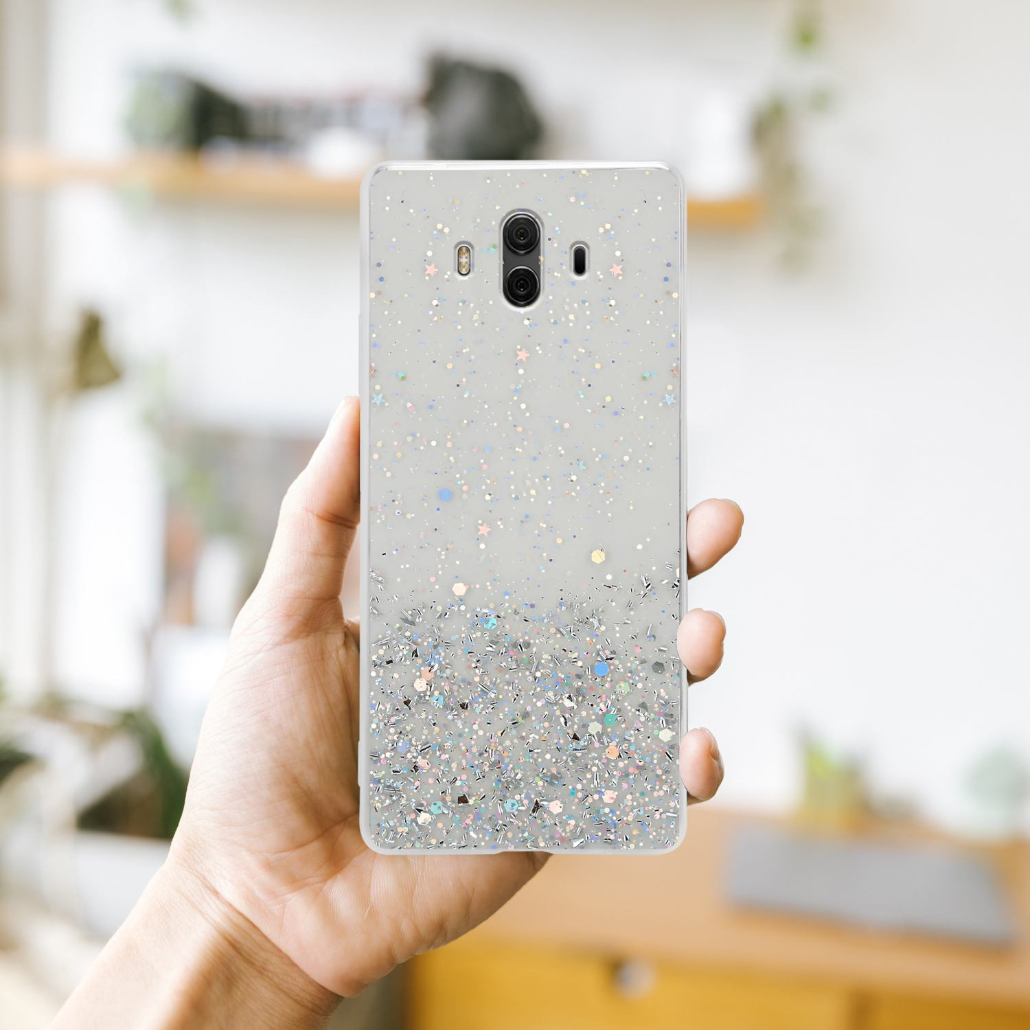 Eine Person hält eine transparente Handyhülle mit Glitzer, vor unscharfem Hintergrund.