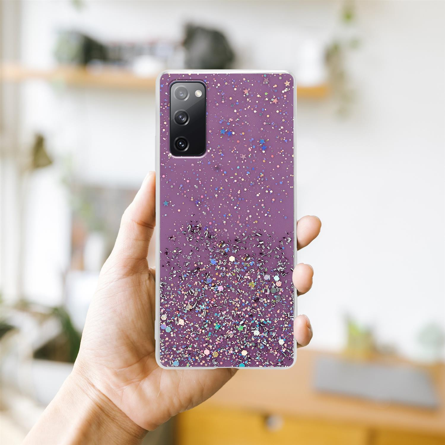 Hand hält Telefon mit lila Hülle und Glitzer. Verschwommener Hintergrund.