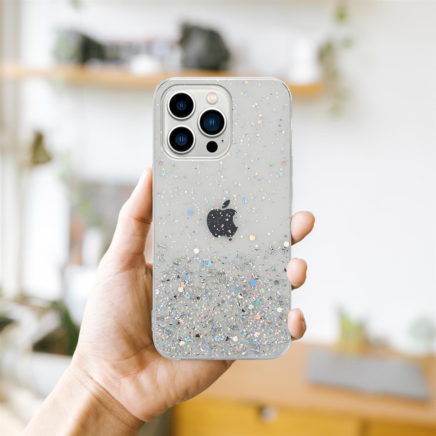 Hand hält eine transparente Handyhülle mit Glitzer. Die Hülle hat das Apple-Logo. Verschwommener Hintergrund.