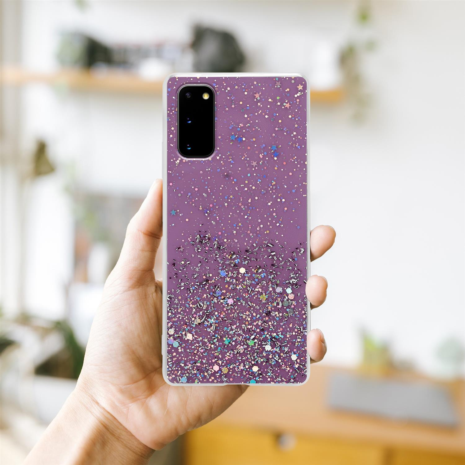 Lila Handyhülle mit Glitzer. Hand hält das Telefon. Hintergrund ist eine verschwommene Innenszene.