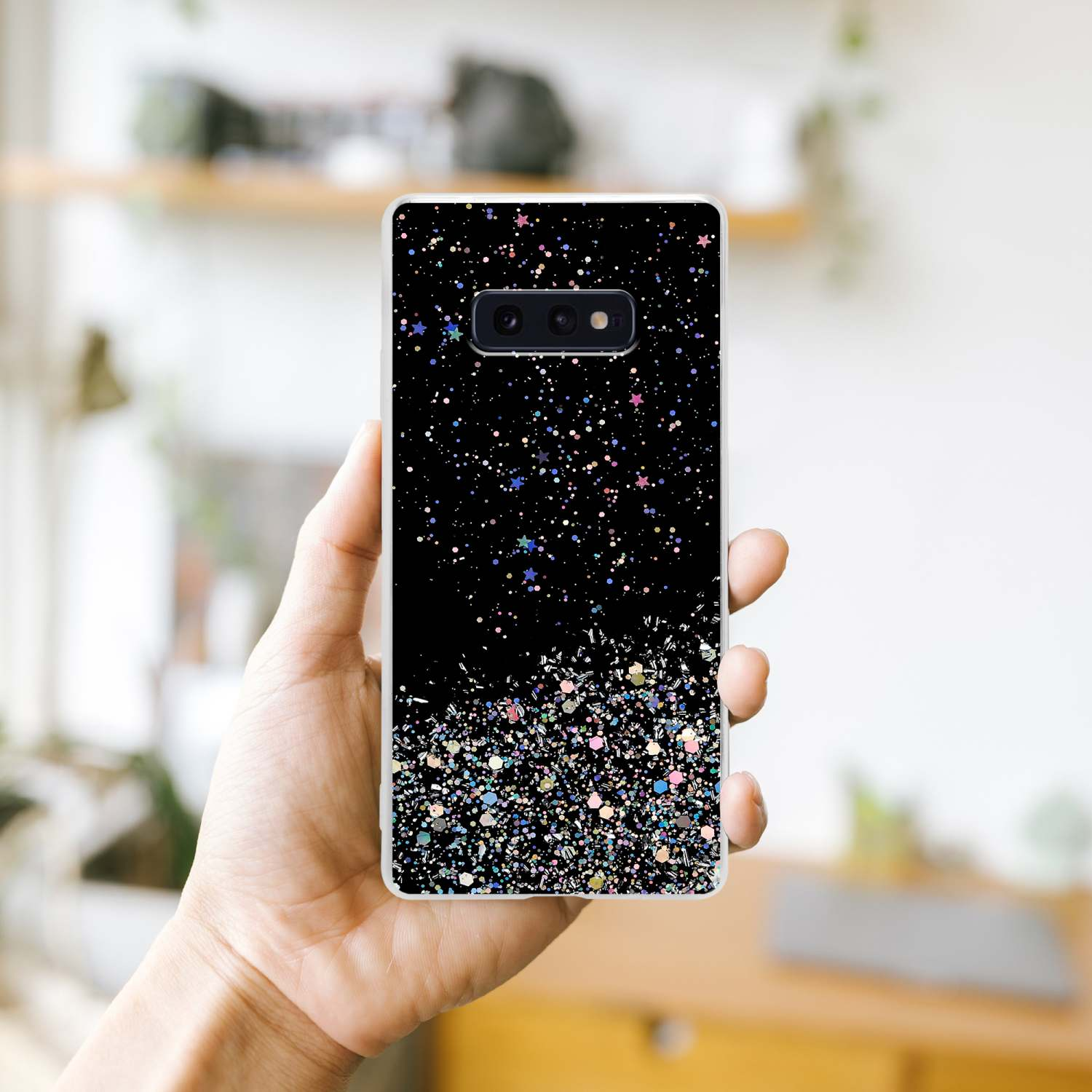Una mano che tiene un telefono con una custodia nera con glitter e uno sfondo nero.