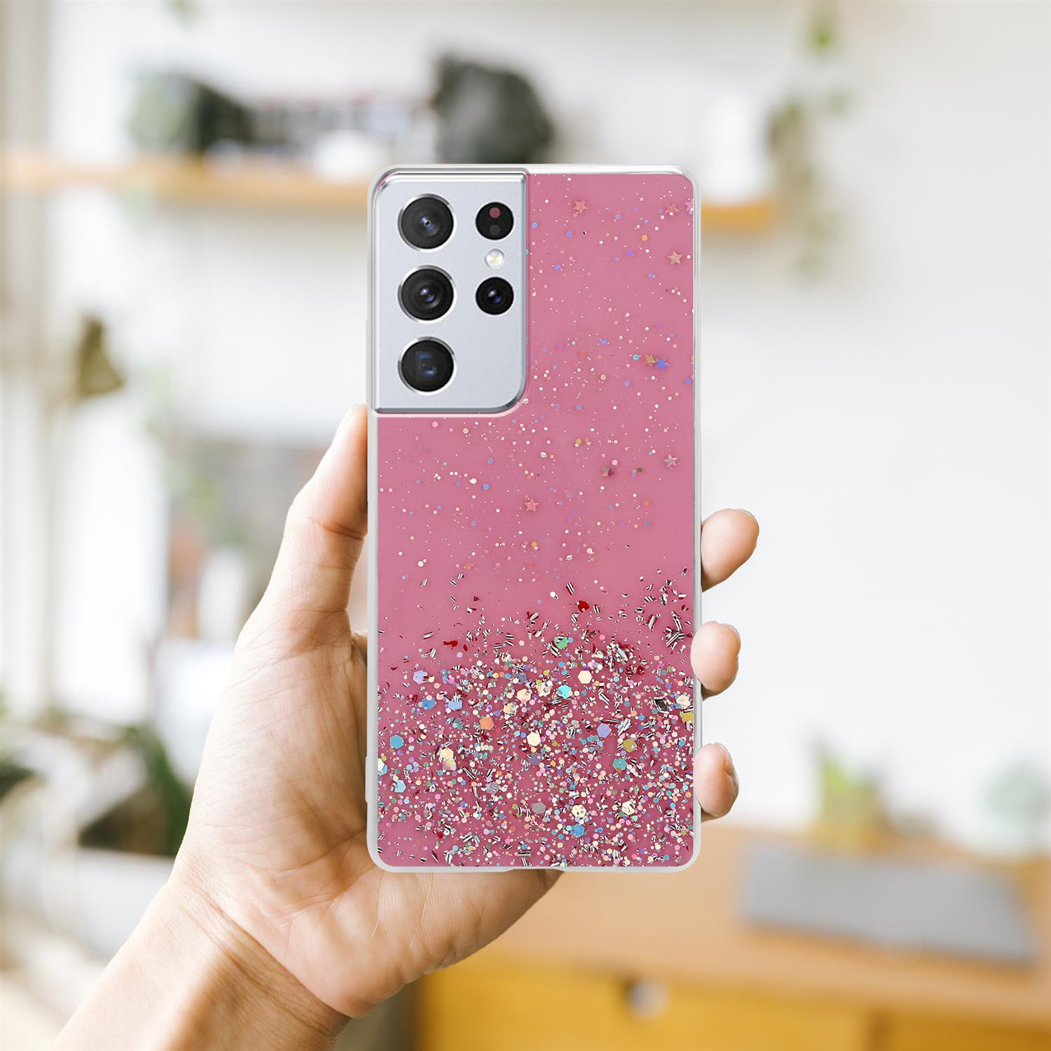 Hand hält eine pinkfarbene Glitzer-Handyhülle. Die Hülle hat Glitzer und einen Kameraausschnitt.