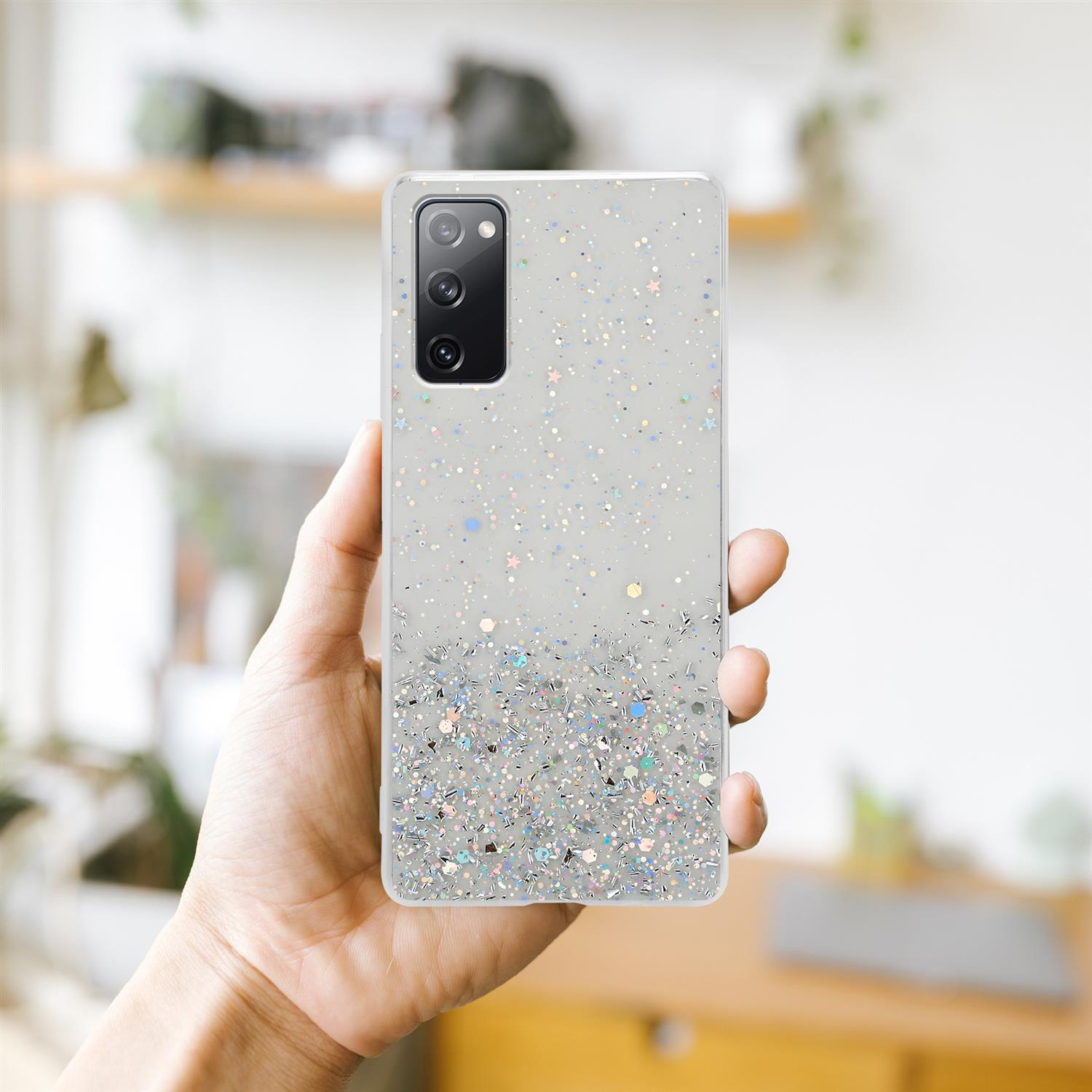 Hand, die ein Telefon mit Glitzerhülle hält. Der Hintergrund ist ein verschwommener Raum.