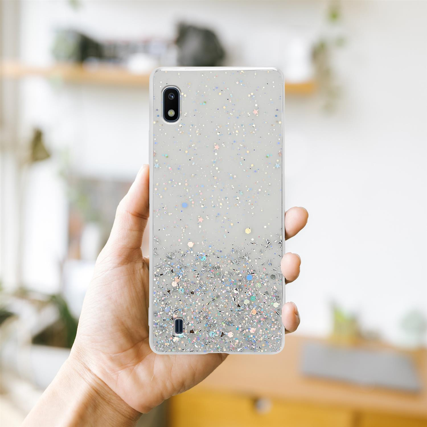 Eine Hand, die eine Handyhülle hält. Die Handyhülle ist transparent mit Glitzer. Der Hintergrund ist unscharf.