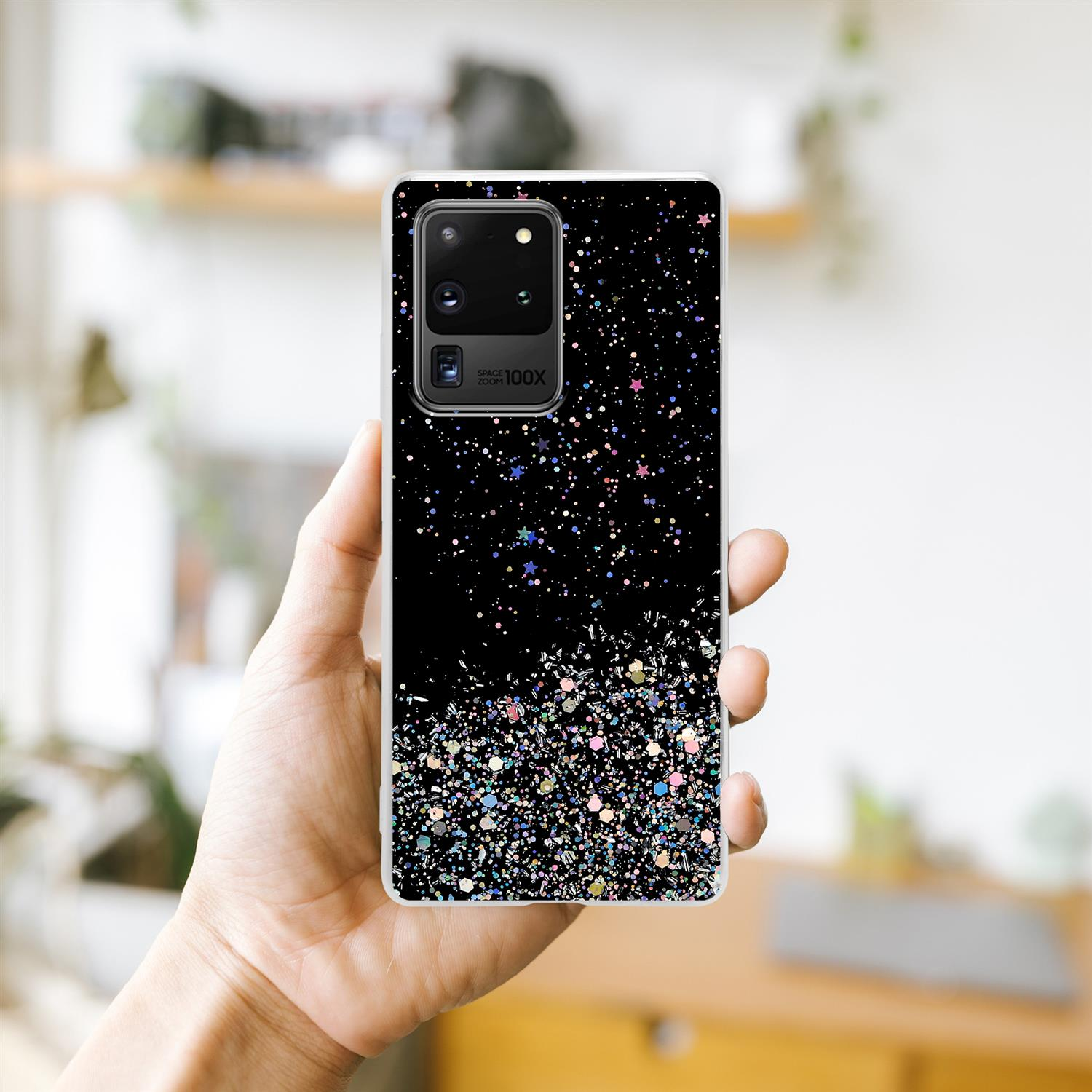Mano che tiene la custodia del telefono con glitter e sfondo nero. La custodia ha una fotocamera con zoom 100x.
