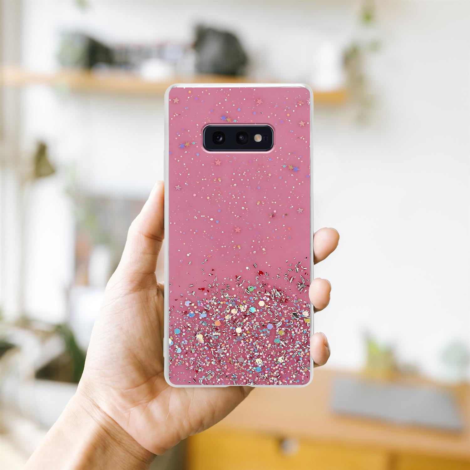 Custodia rosa con glitter, tenuta da una mano, sfondo sfocato.