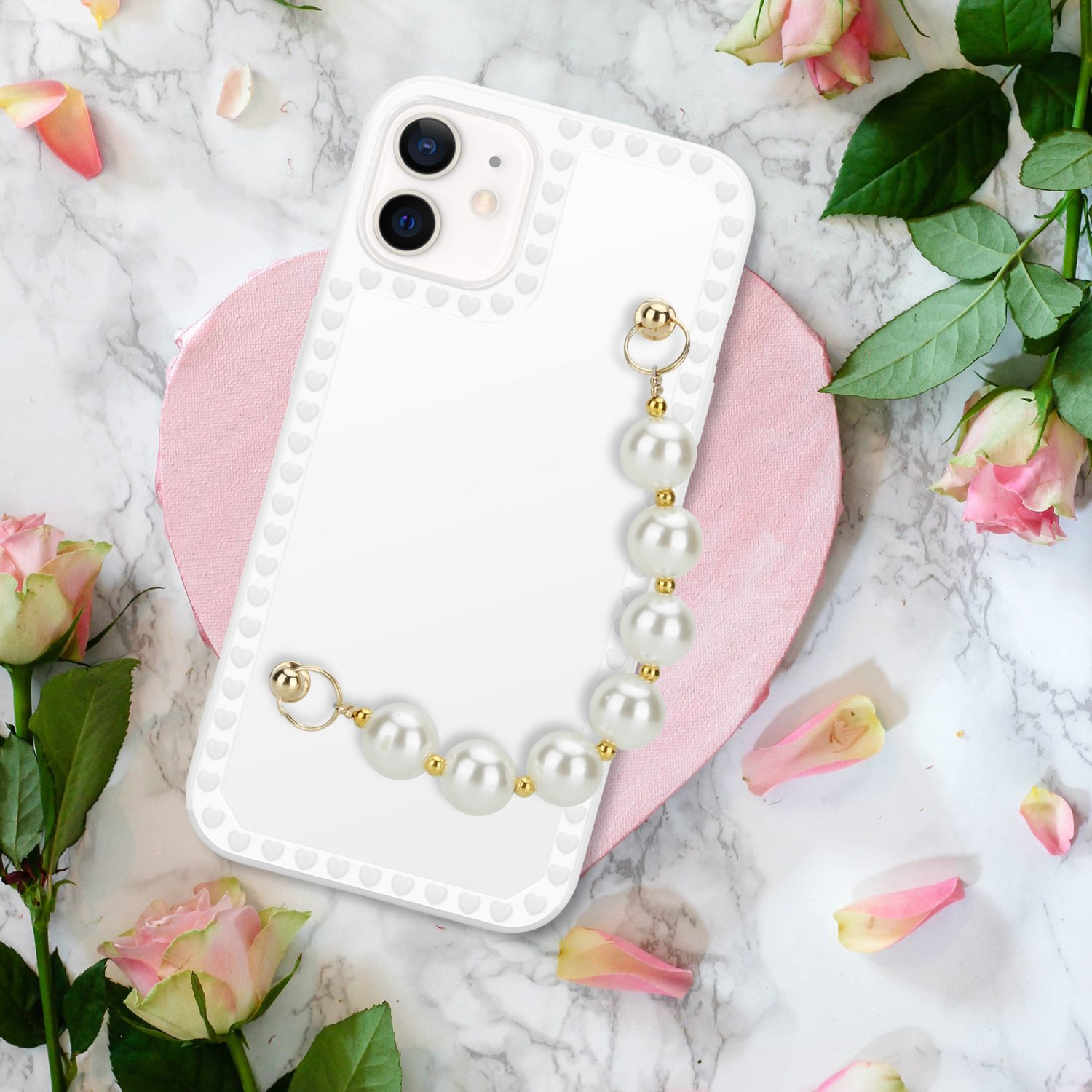 Ein Telefon in einer weißen Hülle mit Herzen, einem Perlenarmband und Rosen auf Marmor.