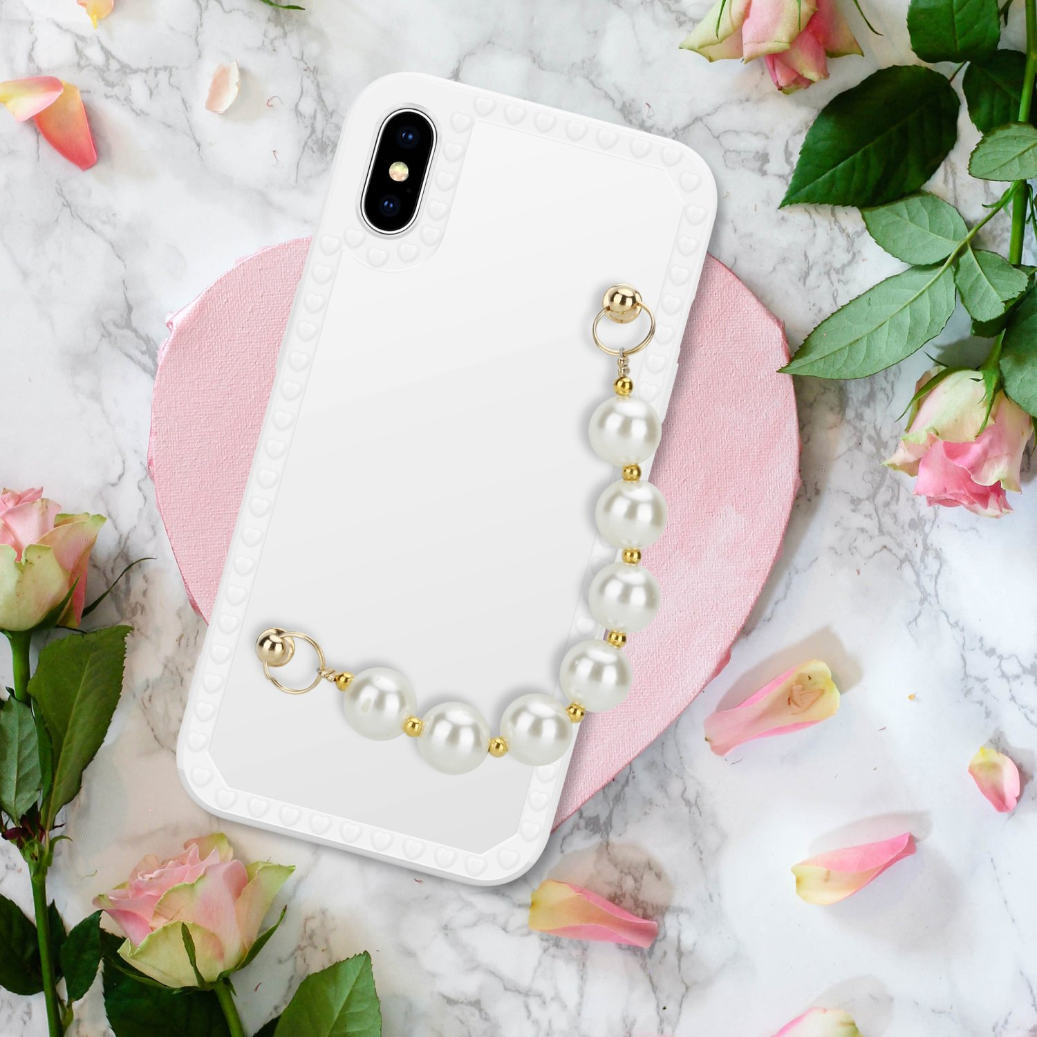 Una custodia bianca per telefono con una catena di perle contro una superficie di marmo con rose e petali.