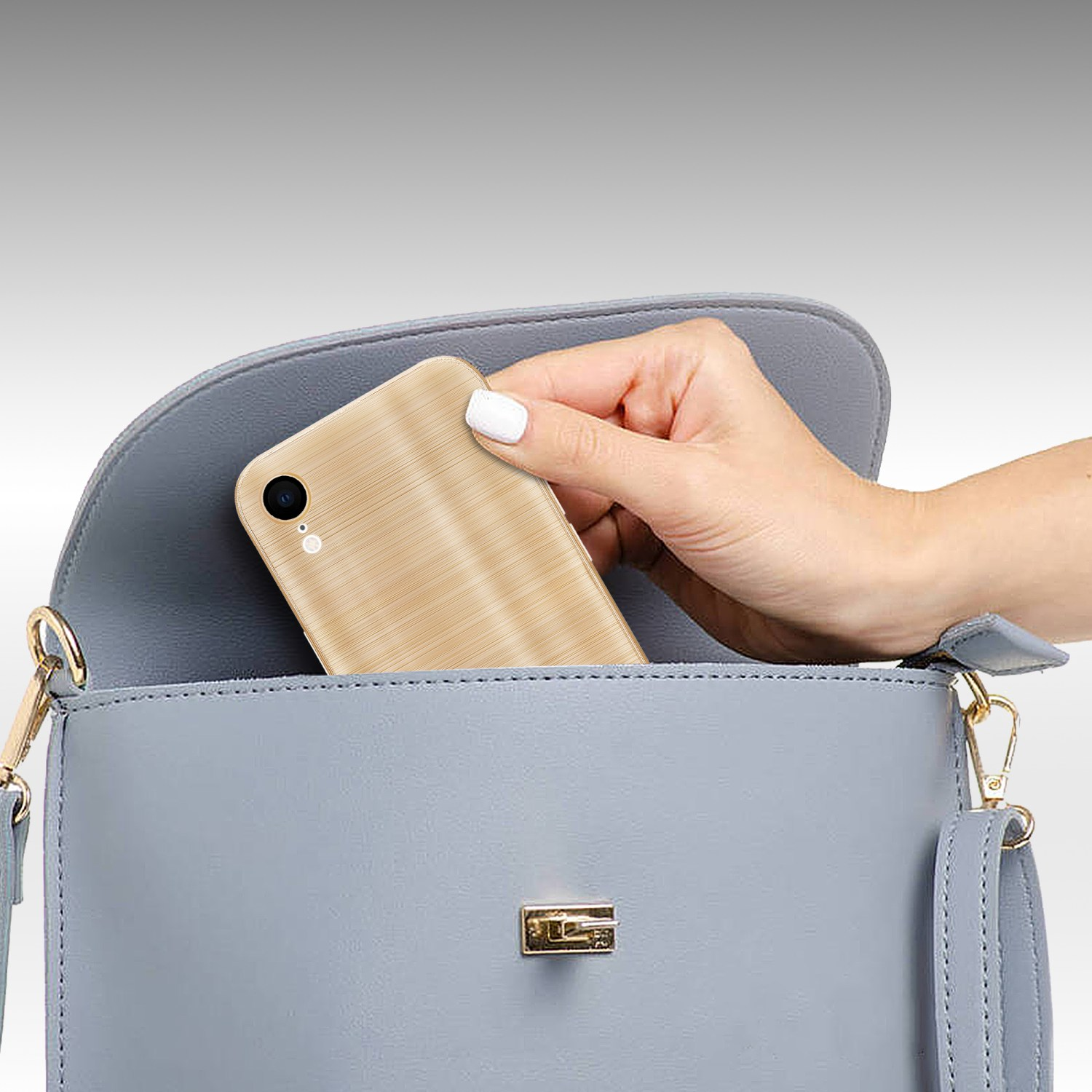 Eine Hand legt ein goldenes Telefon in eine blaue Handtasche. Der Hintergrund ist grau.