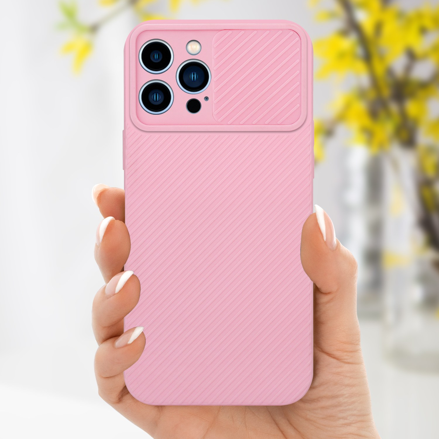 Hand hält rosa Handyhülle mit Kameraabdeckung, Telefon ist rosa. Gelbe Blumen im Hintergrund.