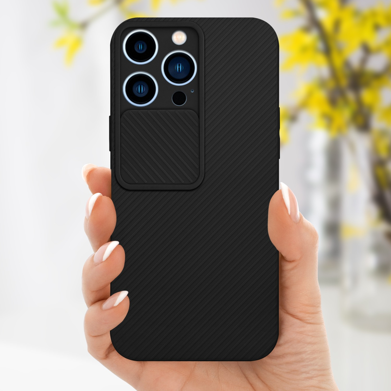 Una mano tiene una custodia nera per telefono con una copertura per la fotocamera. Lo sfondo è un fiore giallo sfocato.
