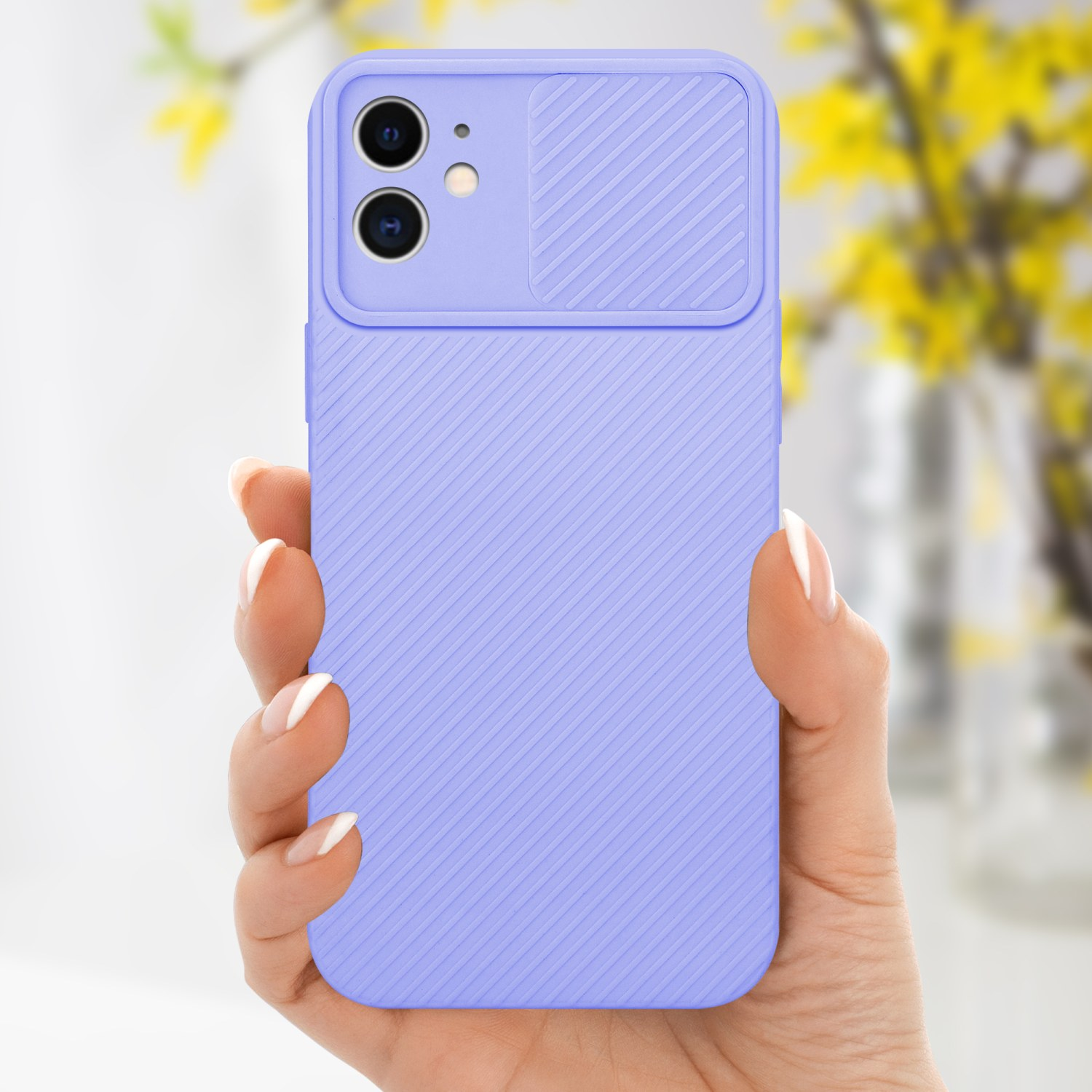 Una mano tiene una custodia viola per telefono. La custodia ha una copertura per la fotocamera. Fiori gialli sullo sfondo.