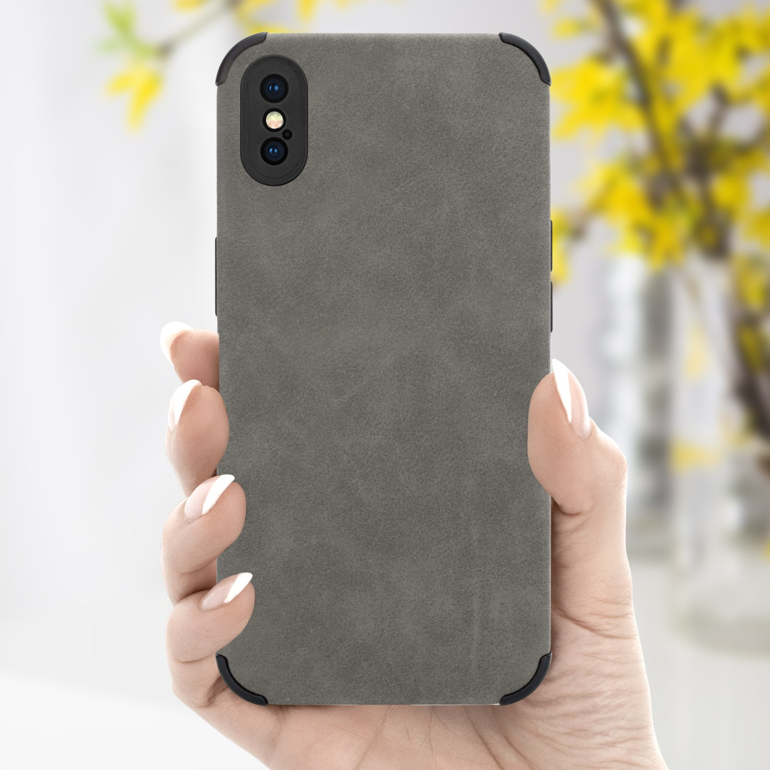 Hand hält eine graue Handyhülle. Der Hintergrund ist ein verschwommenes Interieur mit gelben Blumen.
