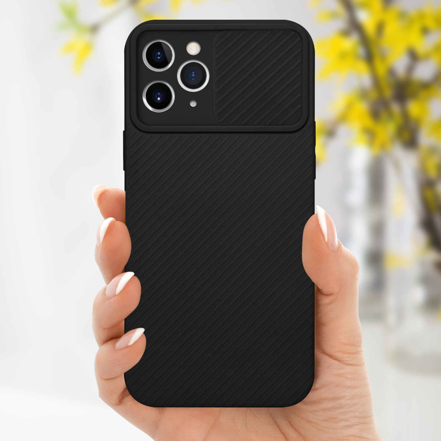 Eine schwarze Handyhülle mit Kameraabdeckung wird von einer Hand gehalten. Gelbe Blumen im Hintergrund.